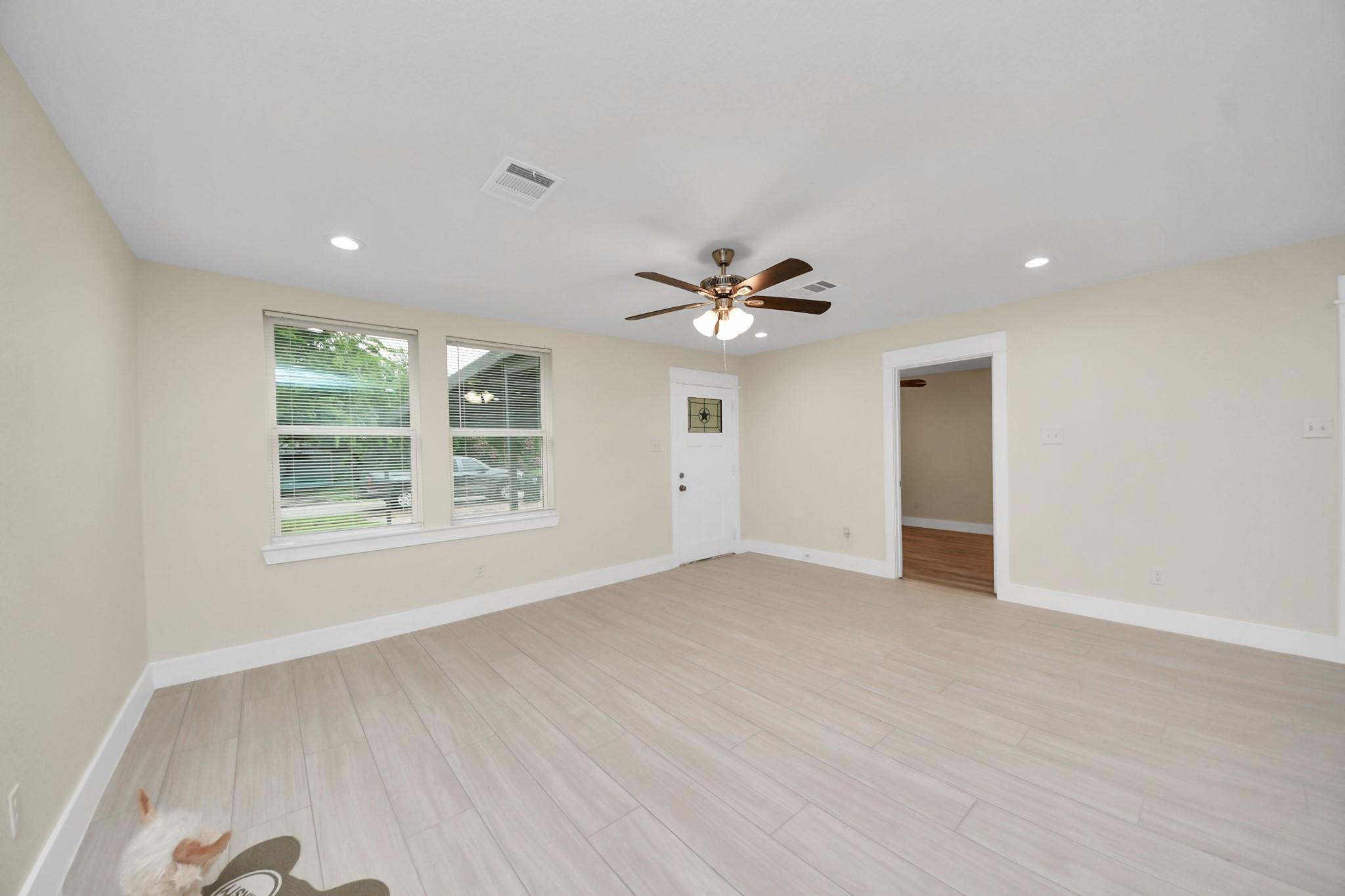 Empty room with light tile floors, two windows, a white entry door, and a ceiling fan.