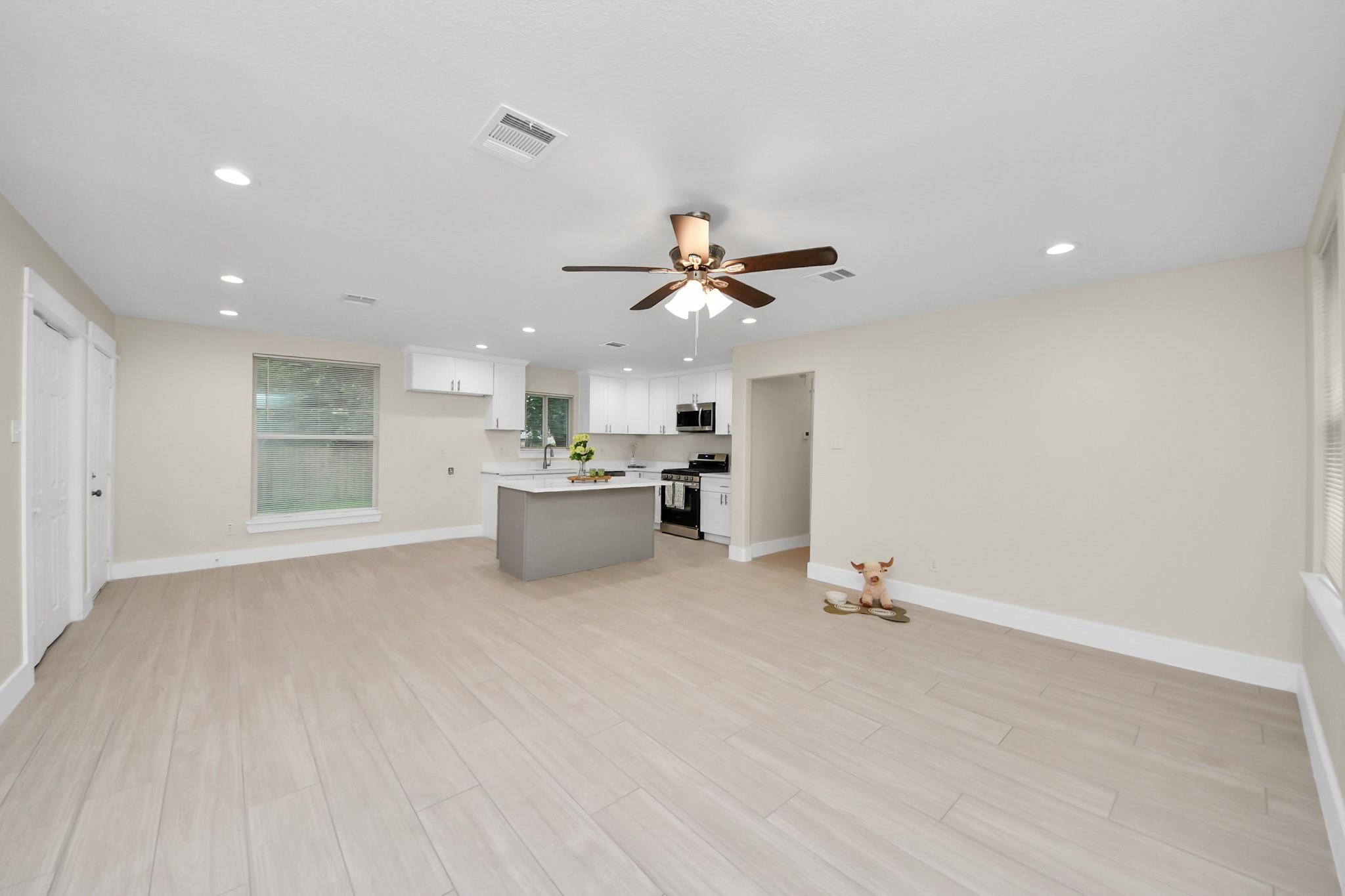 Open-plan kitchen and living area with a gray island, white cabinets, pale tile floors, and ceiling fan.