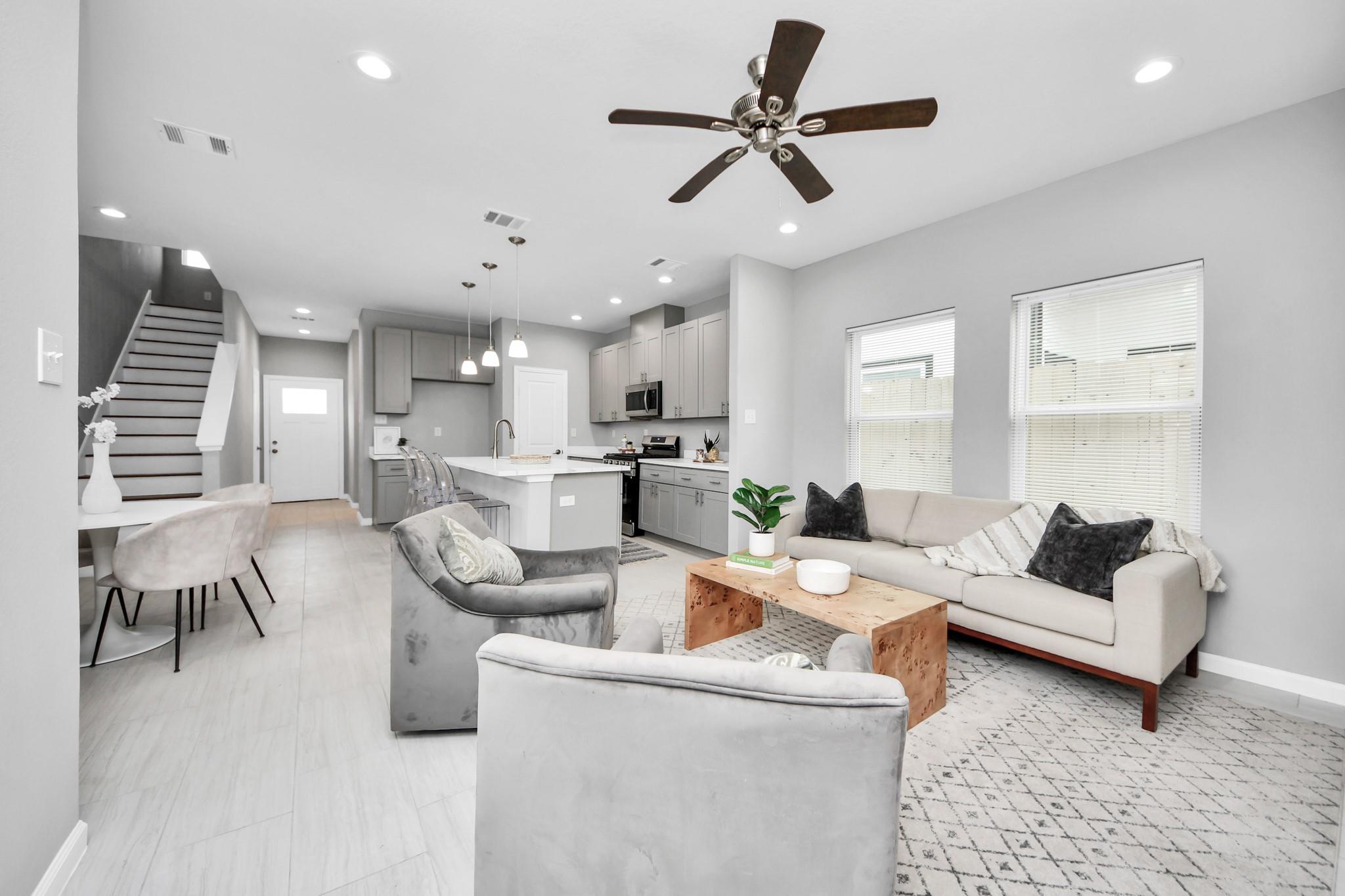 Open-concept living room with a light sofa, gray armchairs, wood coffee table, and kitchen island.
