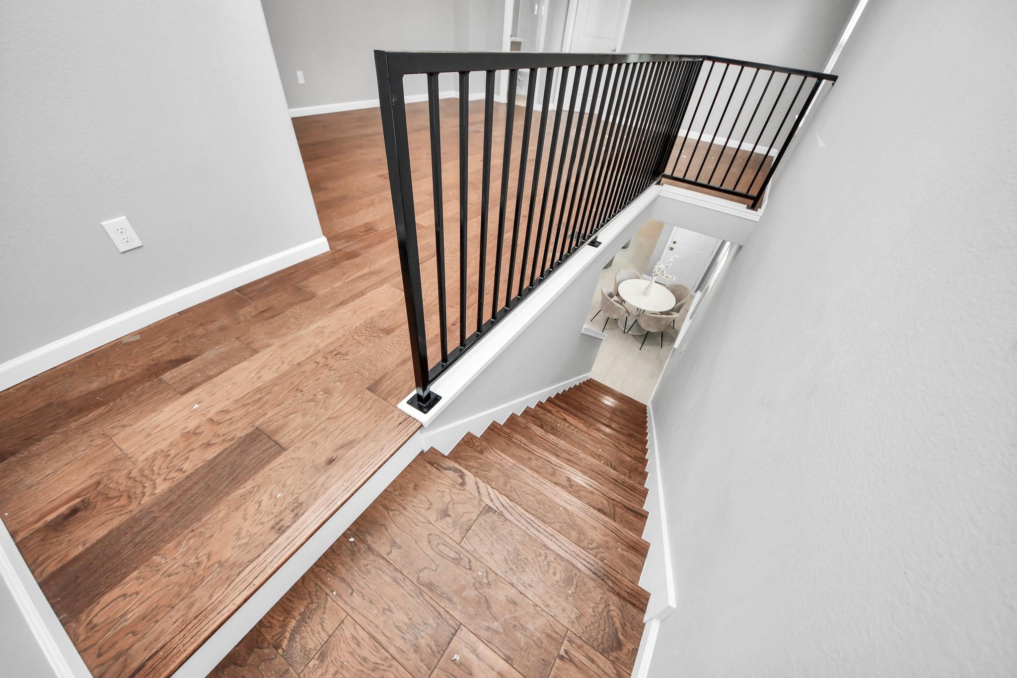 Wooden staircase with black metal railings overlooking a dining area.