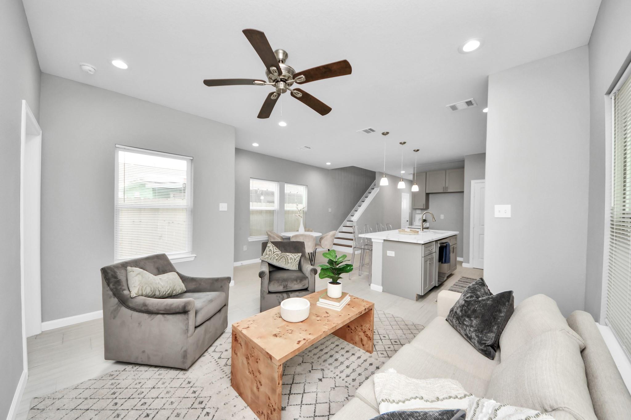 Open-plan living room with gray seating, wood coffee table, kitchen island, and staircase.