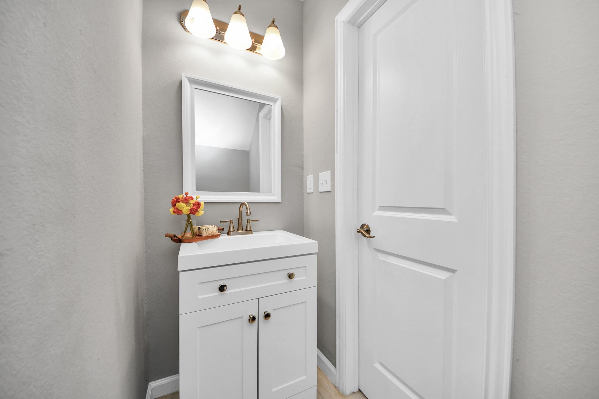 Bathroom vanity with white cabinetry, brass faucet, framed mirror, and flowers on a tray.