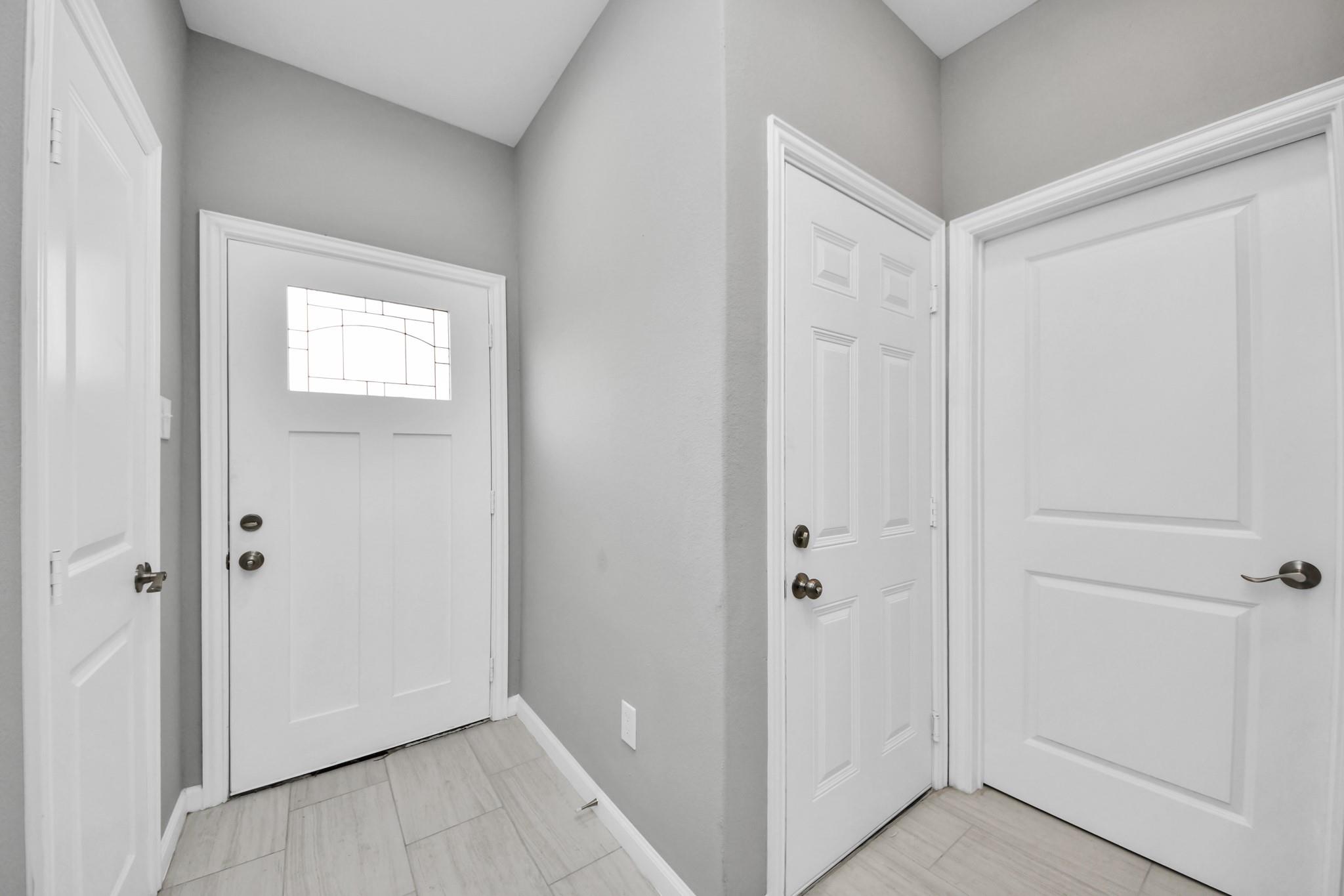 Entry foyer with pale tile flooring and a white front door with decorative glass.