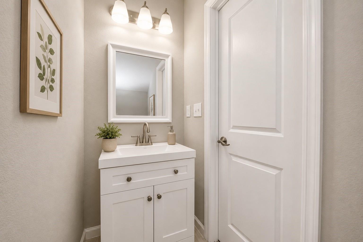 Bathroom vanity with a white paneled cabinet, framed mirror, and botanical wall art.