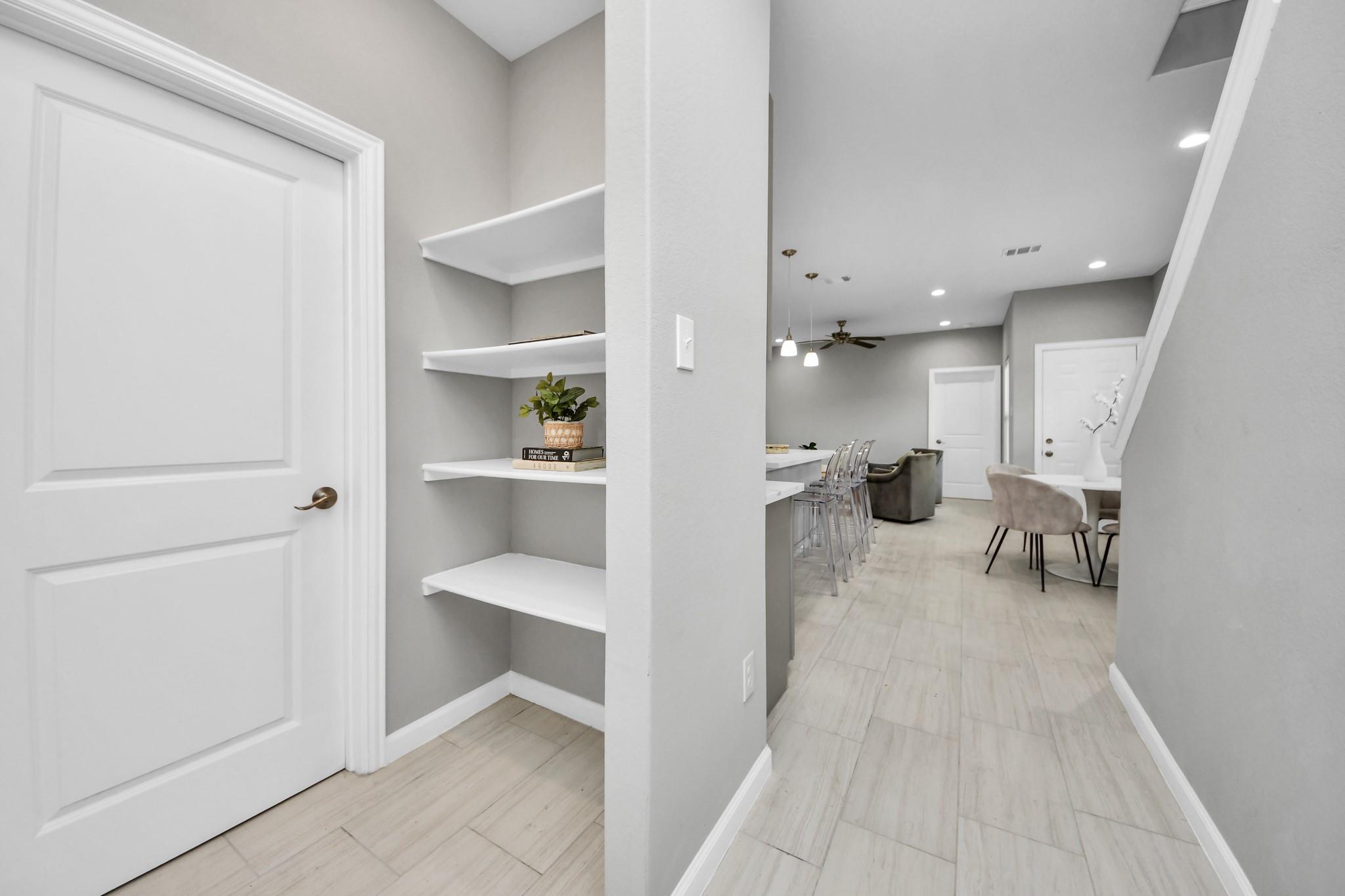 Hallway with built-in floating shelves opens to a dining area and breakfast bar.
