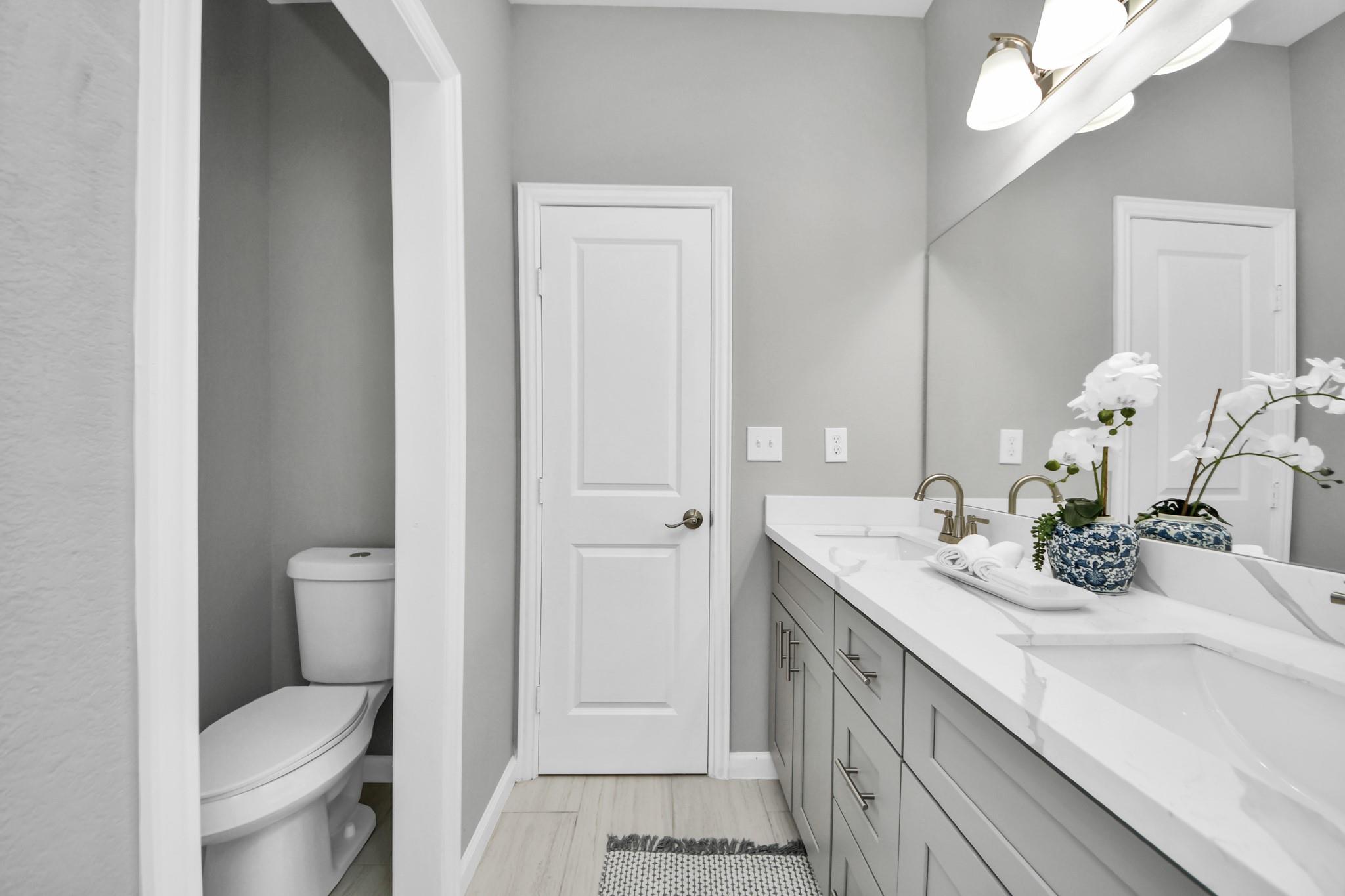 Bathroom with a long double-sink vanity, gray cabinets, and a toilet in a separate alcove.