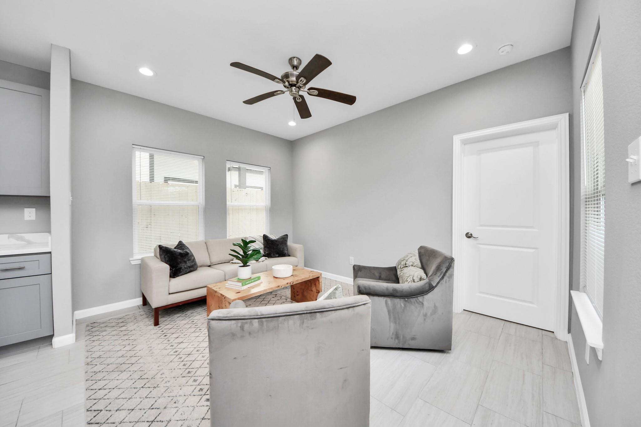 Staged living room with a cream sofa, gray armchairs, and a wood coffee table beneath a ceiling fan.