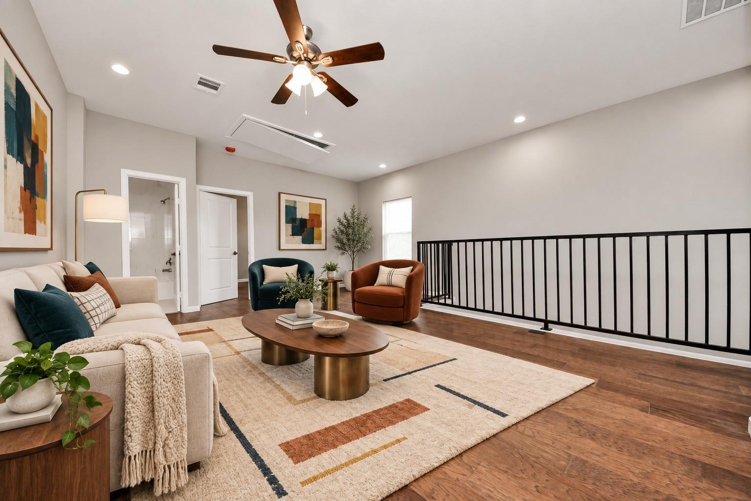 Living room with a cream sofa, teal and rust chairs, and a black railing along the open edge.