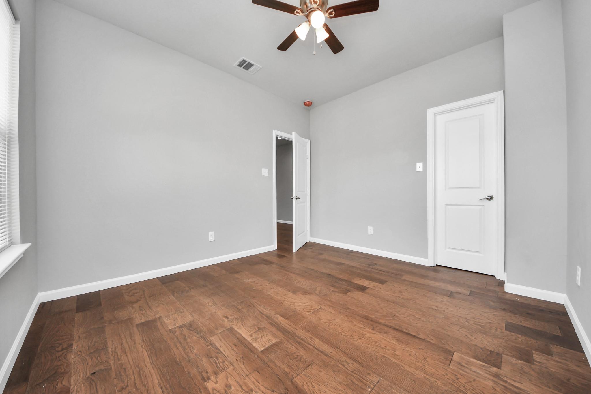 Empty room with gray walls, dark wood floors, a ceiling fan, and two white doors.