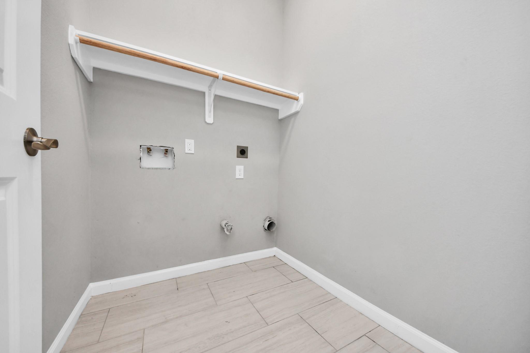 Empty laundry area with washer and dryer hookups, a high shelf and hanging rod, and light tile flooring.