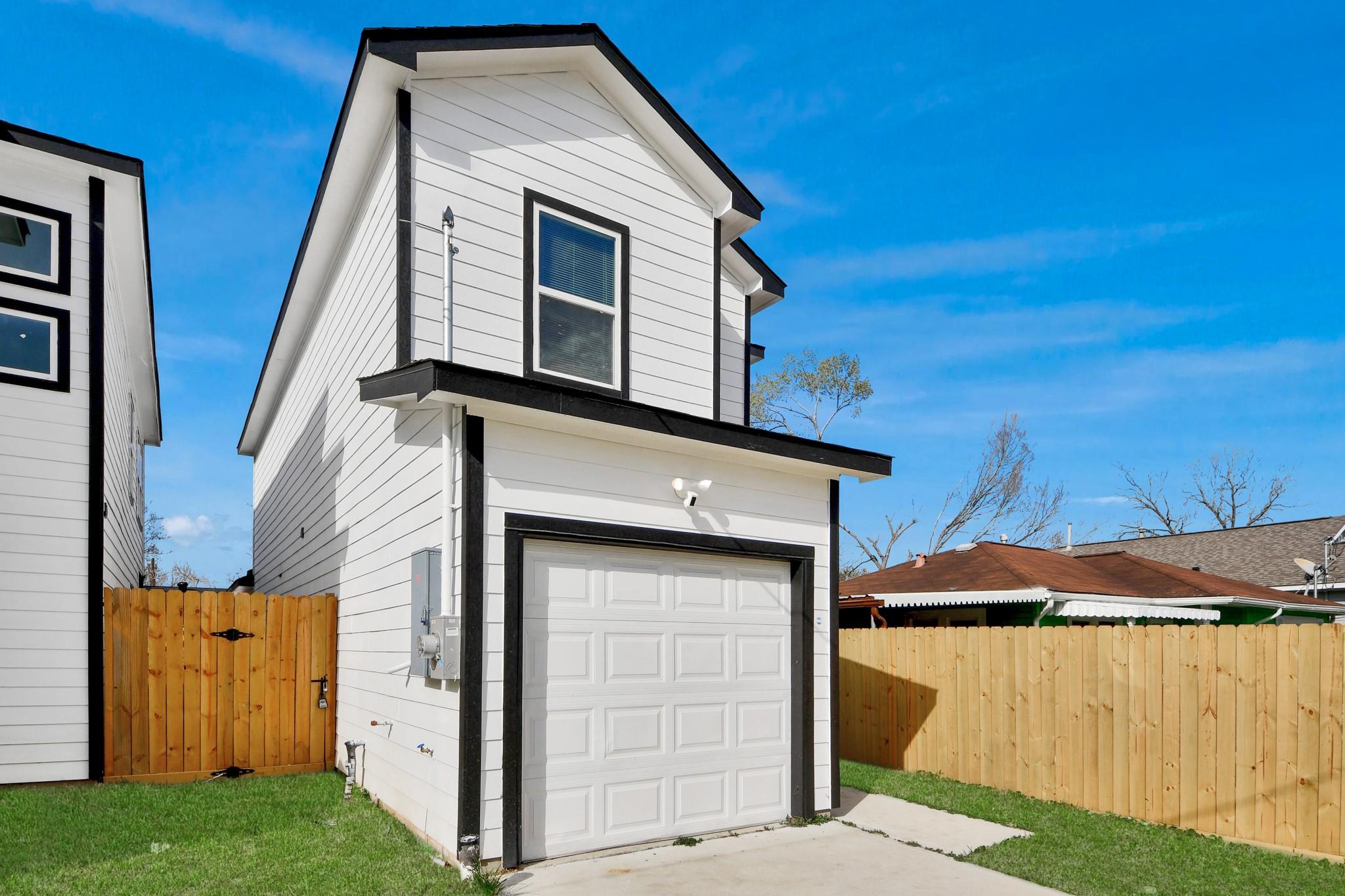 Two-story white house with black trim and attached garage behind a wooden privacy fence.