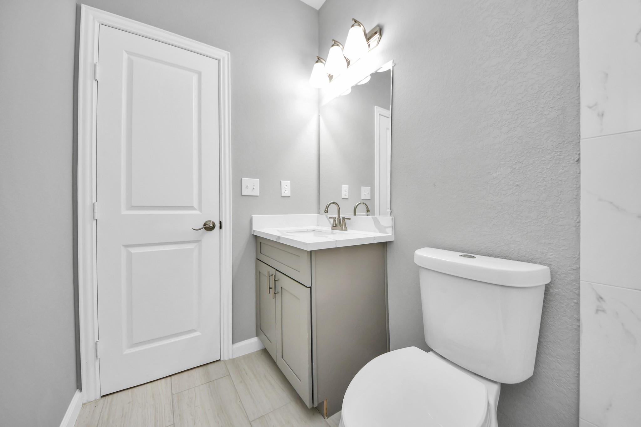 Bathroom with a gray vanity, white countertop, large mirror, and toilet.