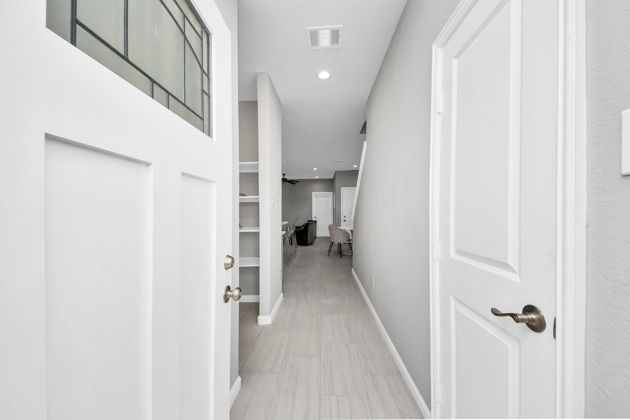 Bright tiled hallway leading toward a dining and living area, framed by white doors and built-in shelving.