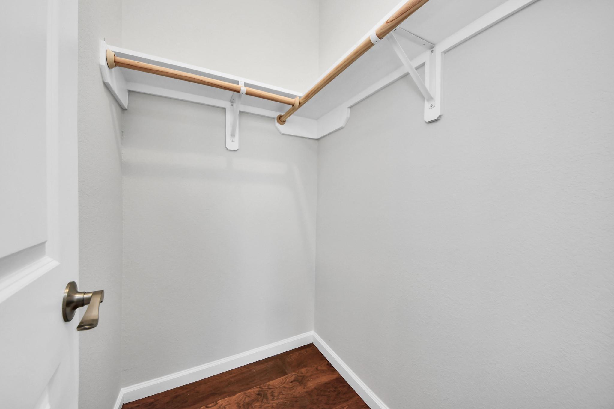 Empty walk-in closet with a wooden hanging rod and dark wood flooring.