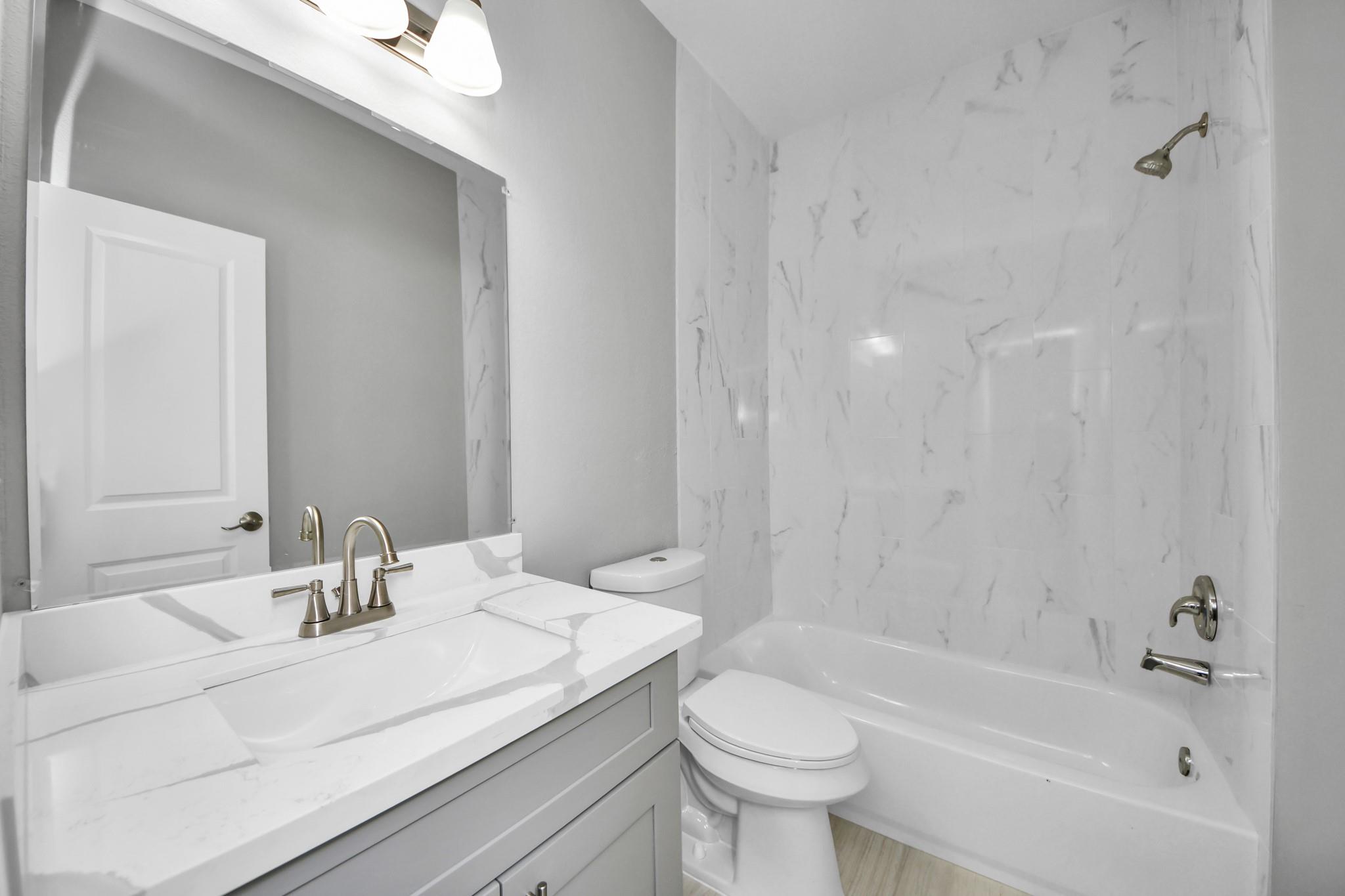 Bathroom with a white vanity, toilet, and bathtub with marble-look surround.