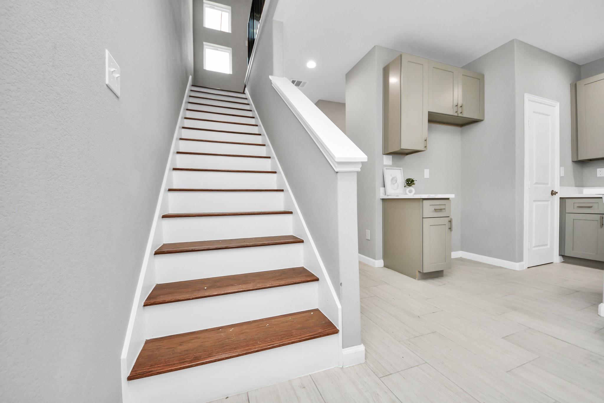 Staircase with dark wood treads beside a light-cabinet kitchen.