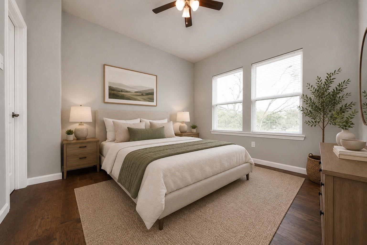 Staged bedroom with a white bed, muted green throw, and two large windows.