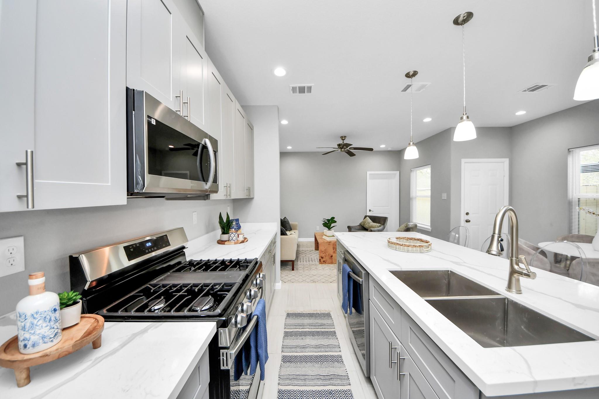 Bright white kitchen with a large sink island, stainless steel range, and open living area.