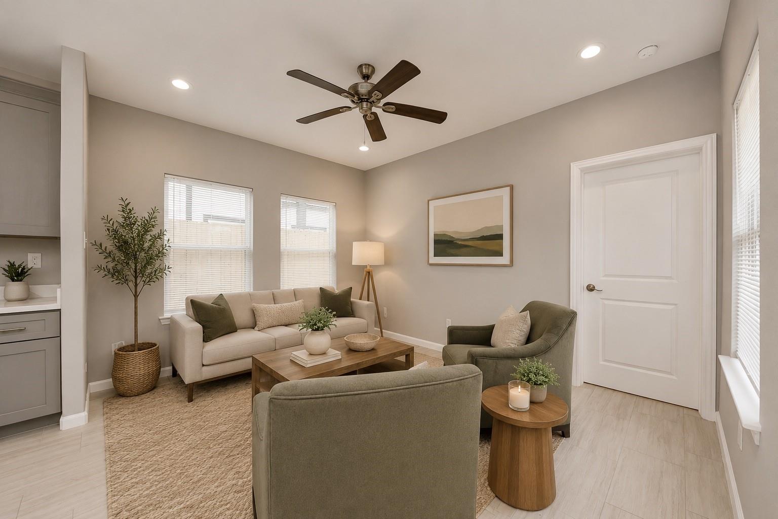 Staged living room with neutral seating, a wood coffee table, and a ceiling fan.