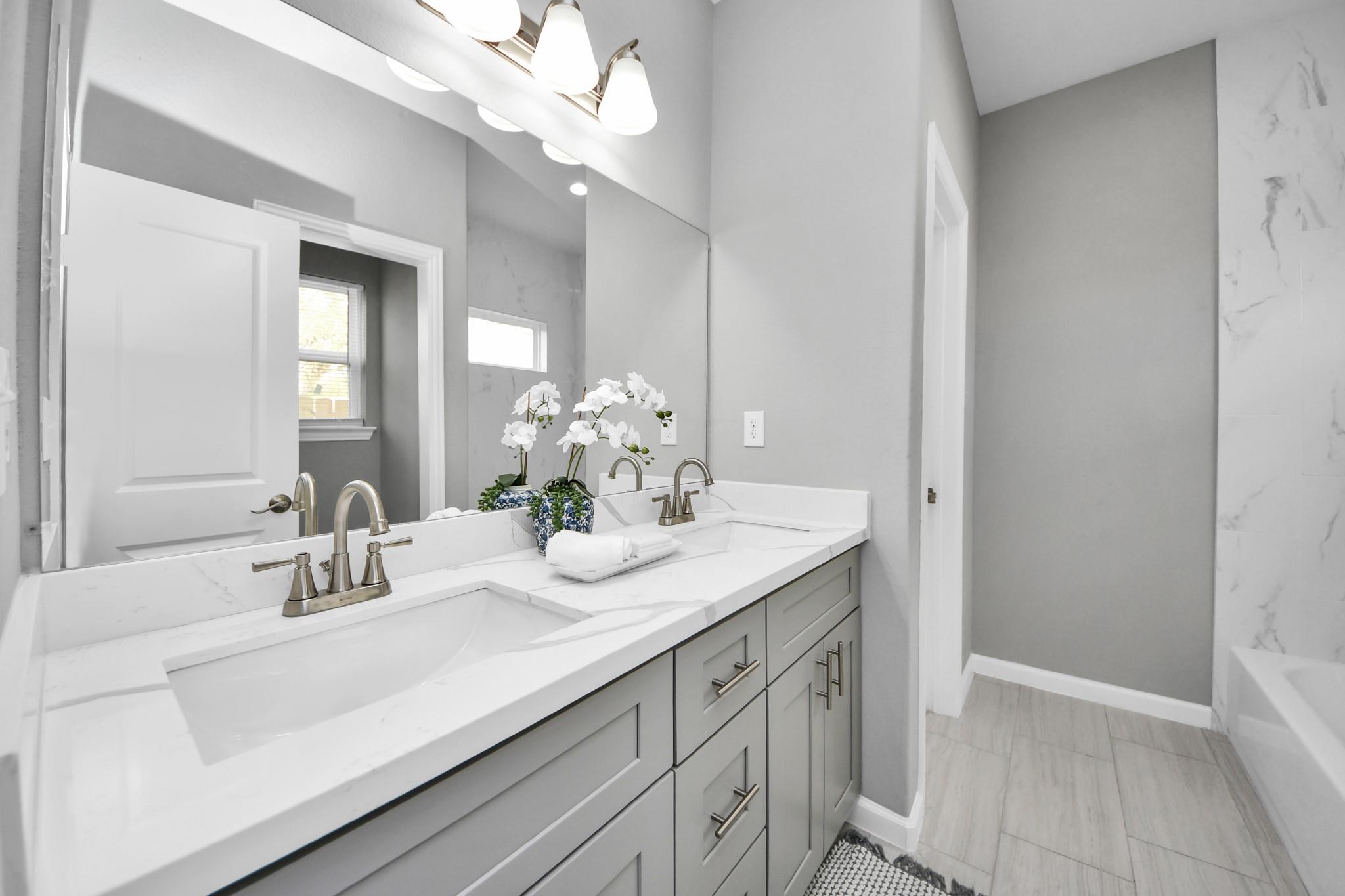 Bathroom with a double-sink vanity, white counters, gray cabinets, and a large mirror.