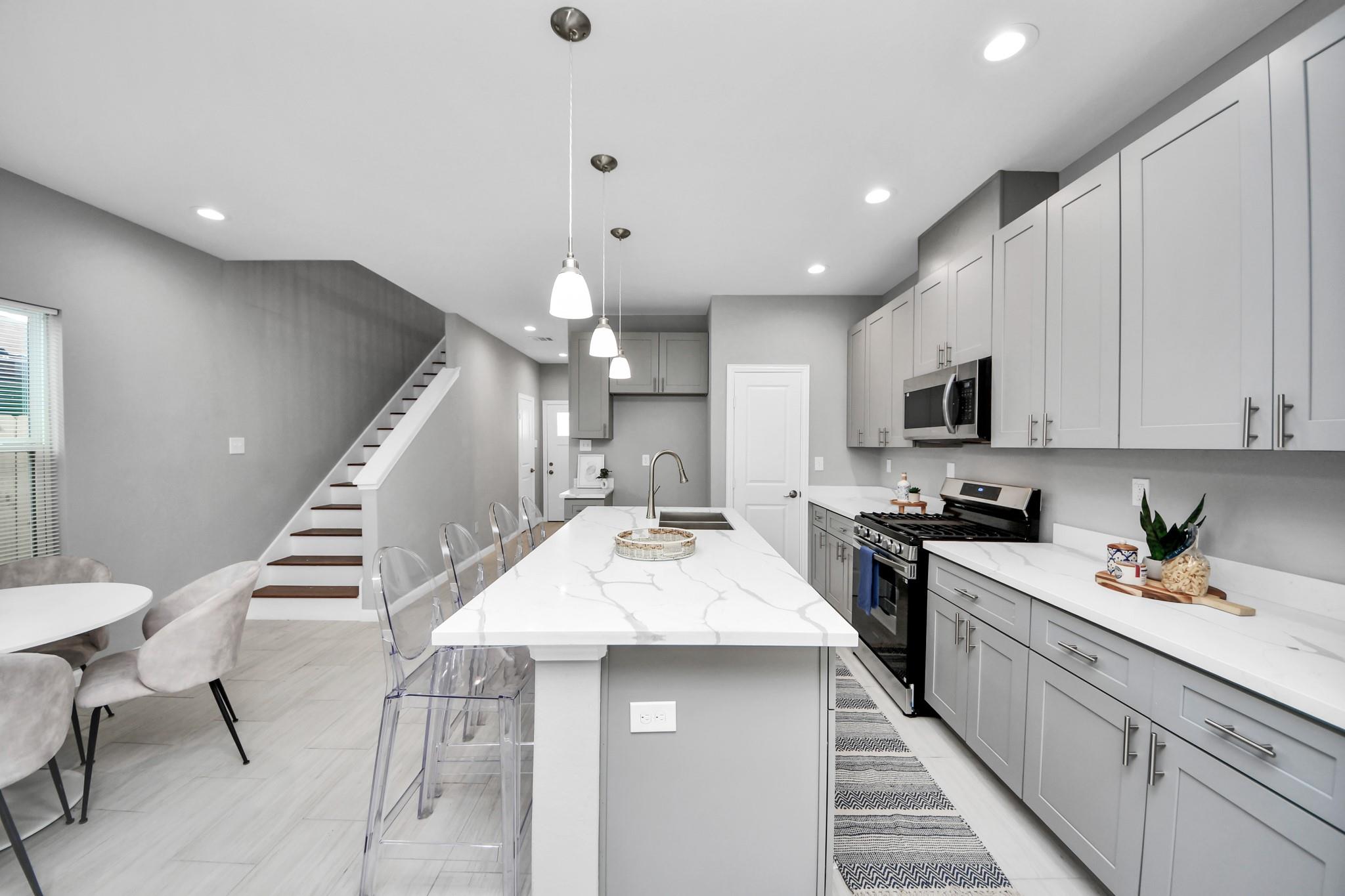 Modern kitchen with a white veined island, gray cabinets, stainless steel appliances, and an adjacent staircase.