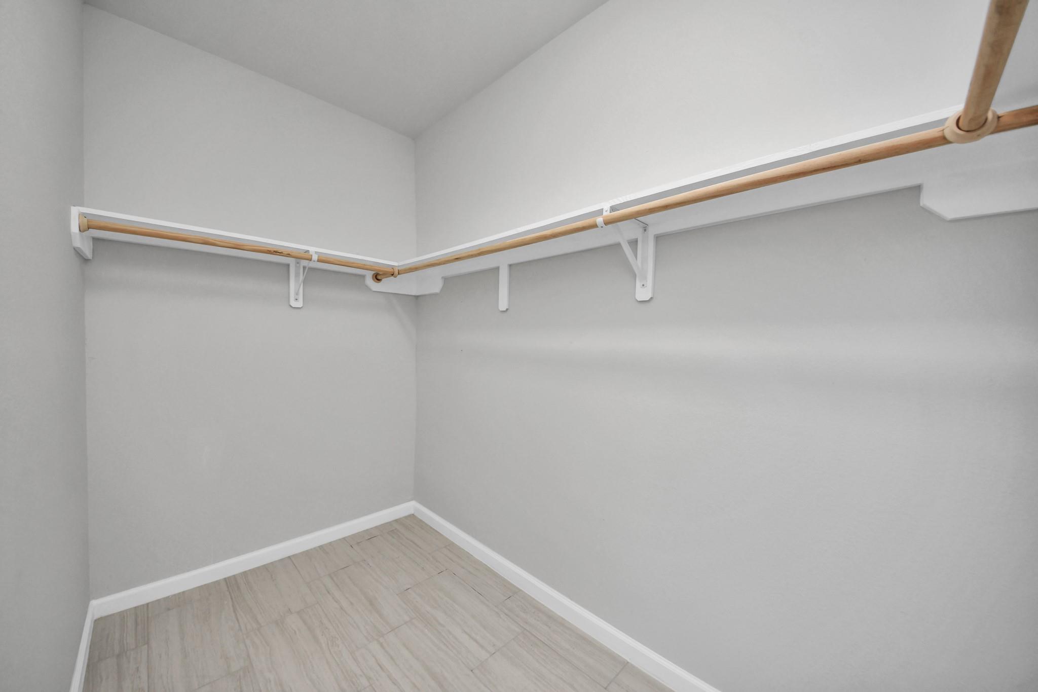 Empty walk-in closet with wooden clothes rods and pale tile flooring.