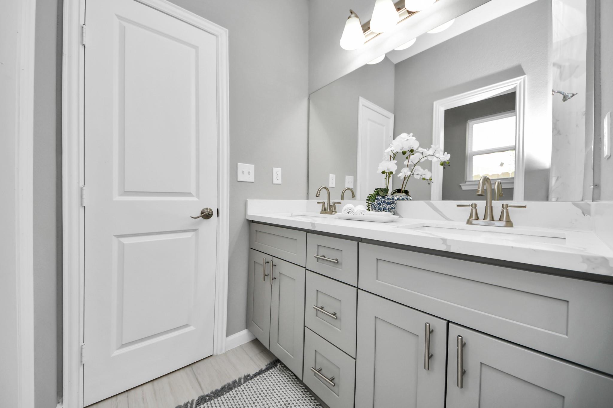 Bathroom with a double vanity, gray cabinets, brass-toned faucets, and a large mirror.