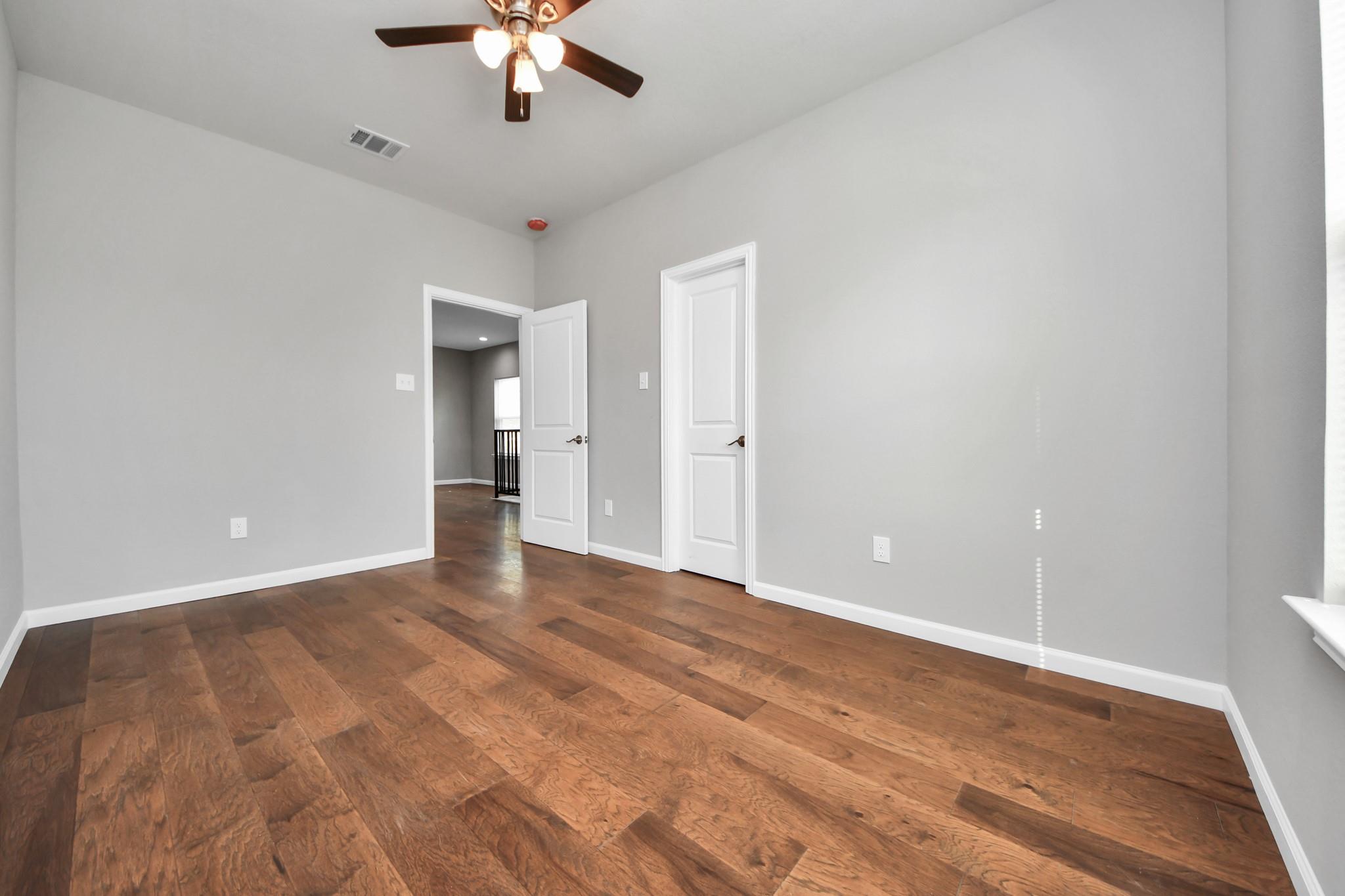 Empty room with hardwood floors, gray walls, two doors, and a ceiling fan.
