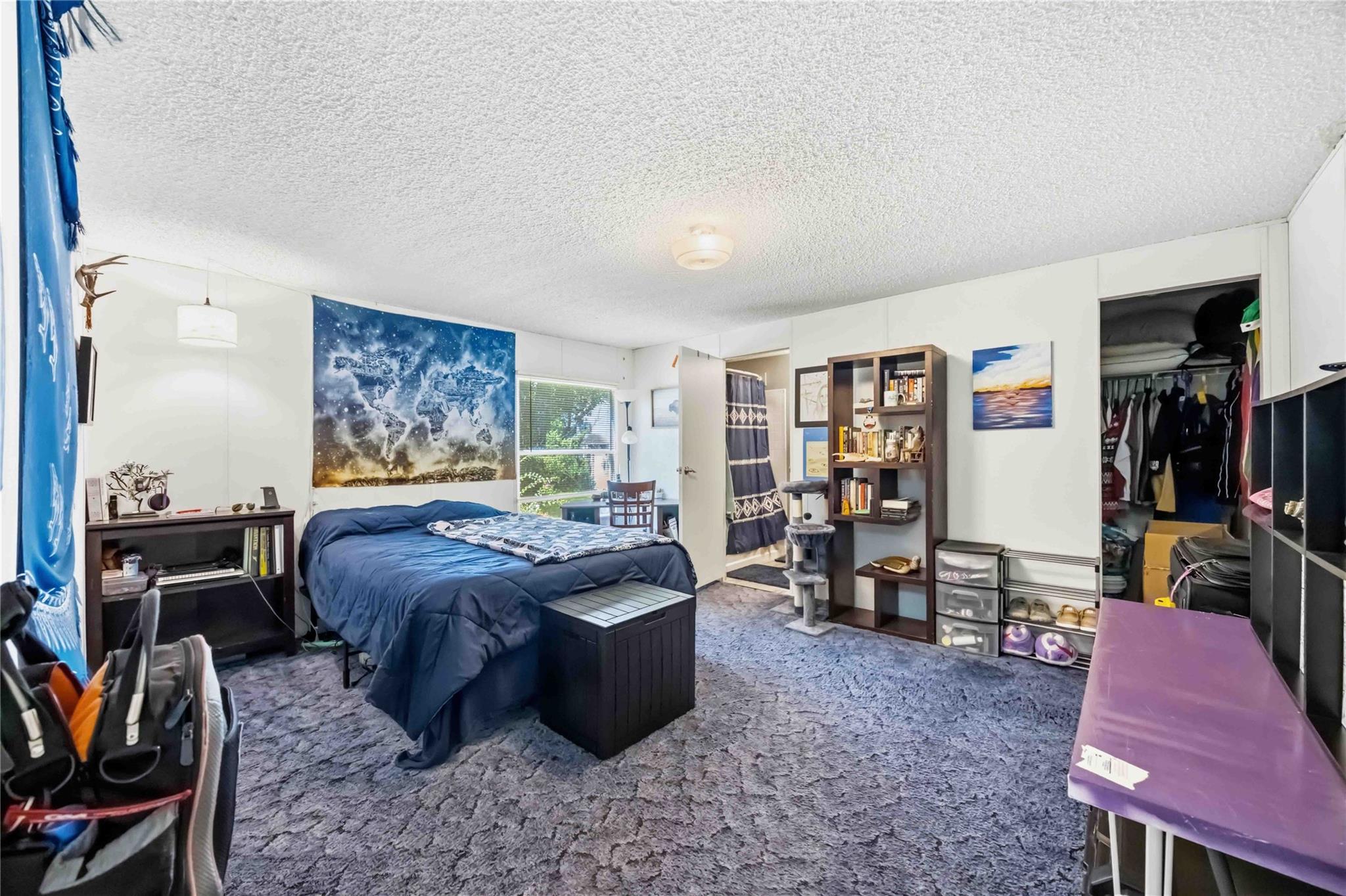 Bedroom with a blue bed beneath a space-themed tapestry, open closet, and bookcase.