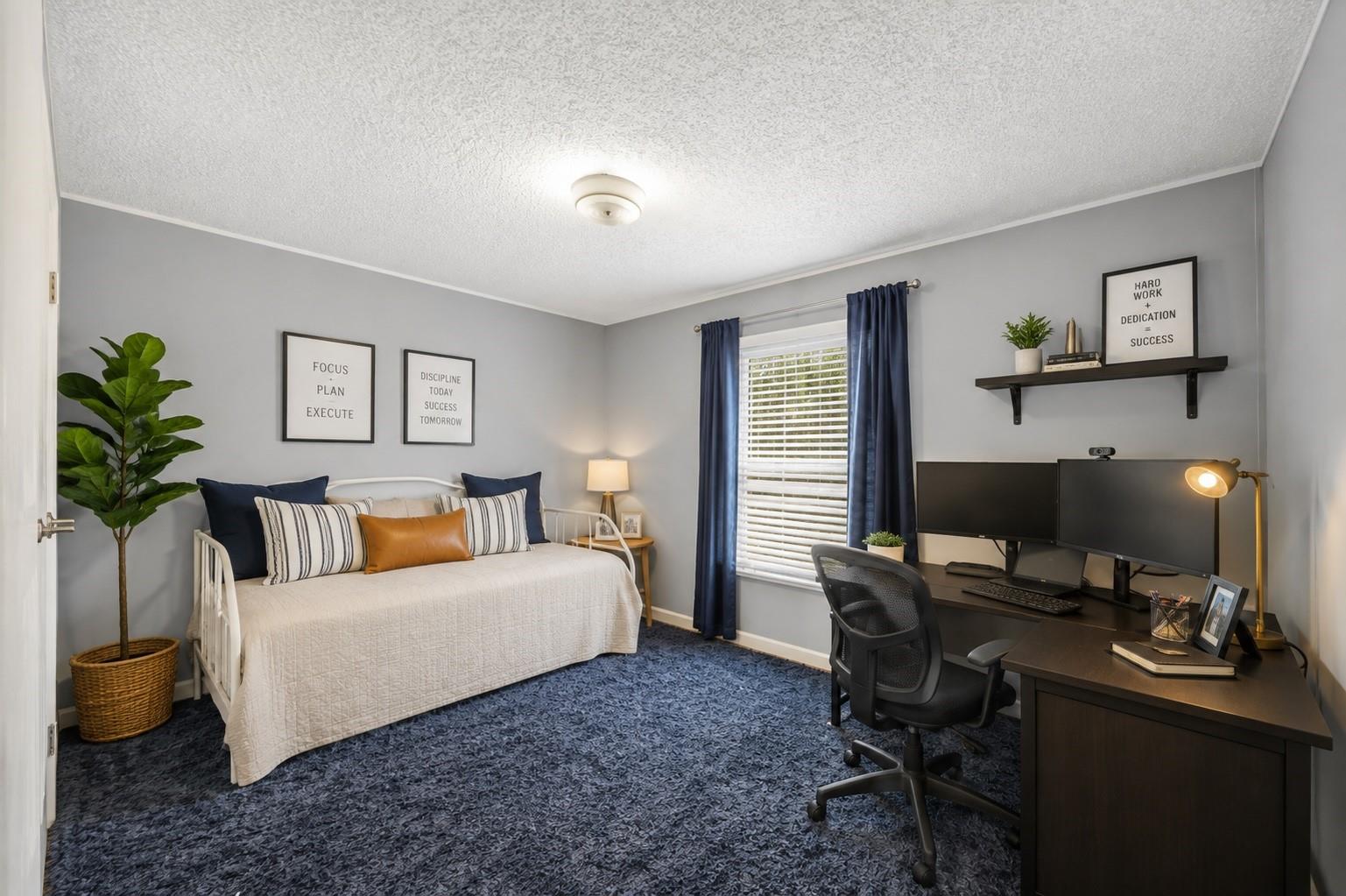 Bedroom home office with a white daybed, dual-monitor desk, and blue curtains.