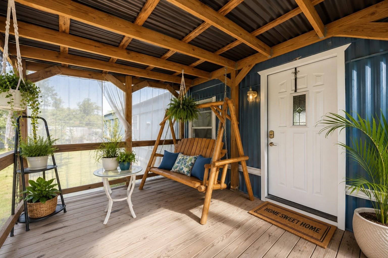 Covered front porch with a wooden swing, exposed beams, potted plants, and a white entry door.