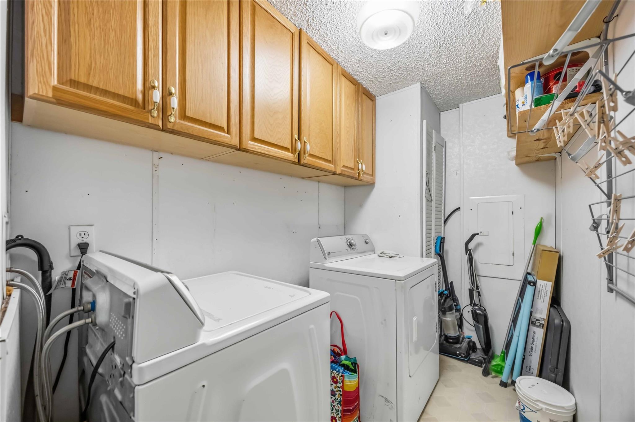 Laundry room with washer and dryer beneath wooden cabinets, plus cleaning supplies and storage.