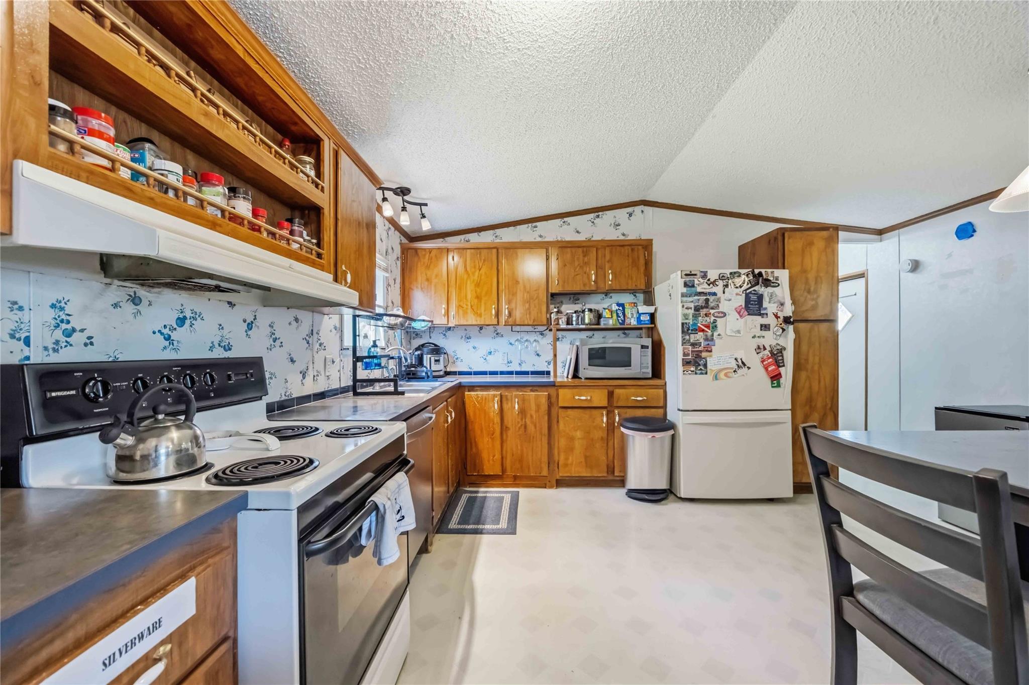 Kitchen with honey-colored wood cabinets, open spice shelves, and blue floral wallpaper.