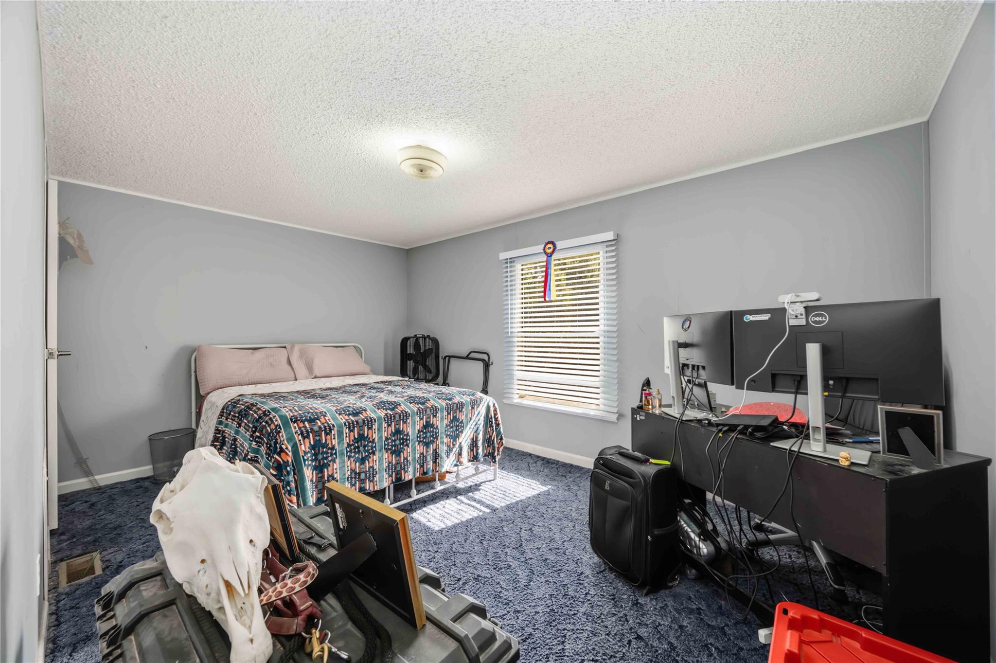 Bedroom with a bed, blue carpet, and computer workstation beneath a window.