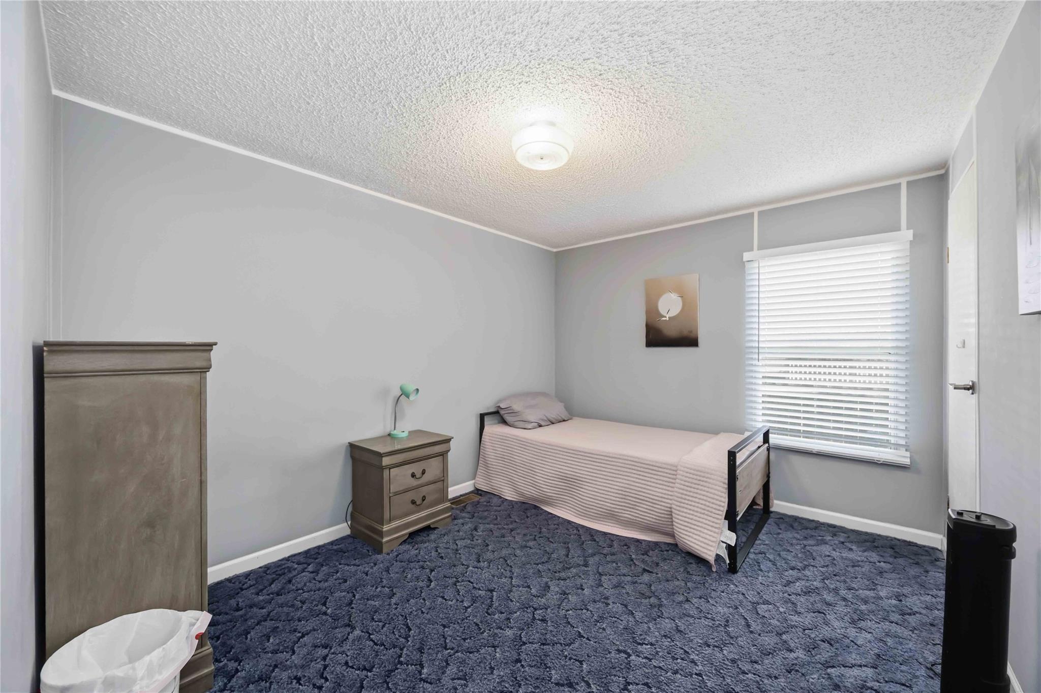 Bedroom with a single bed, wooden furniture, white blinds, and dark blue carpet.