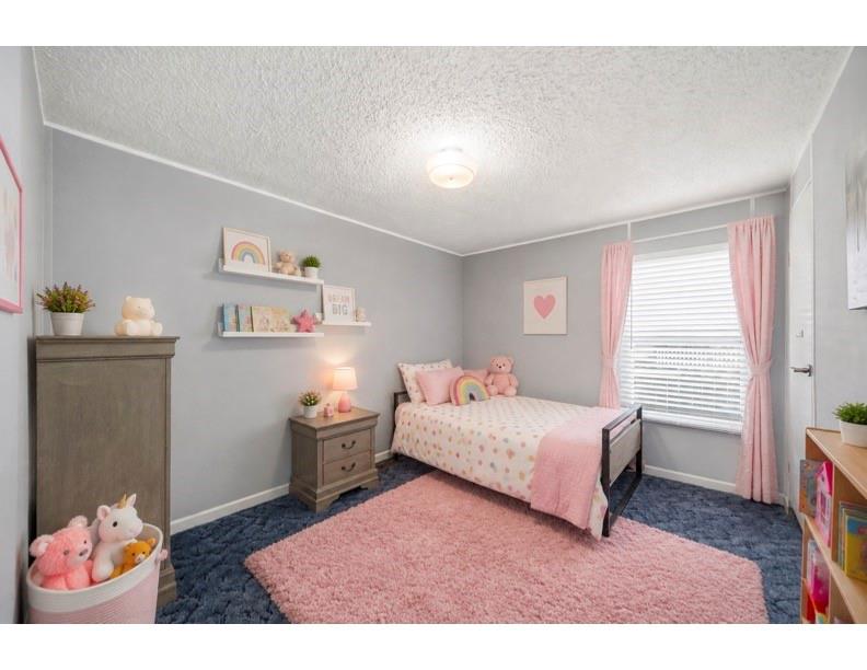 Bedroom with a pink bed and rug, navy carpet, and stuffed animals.