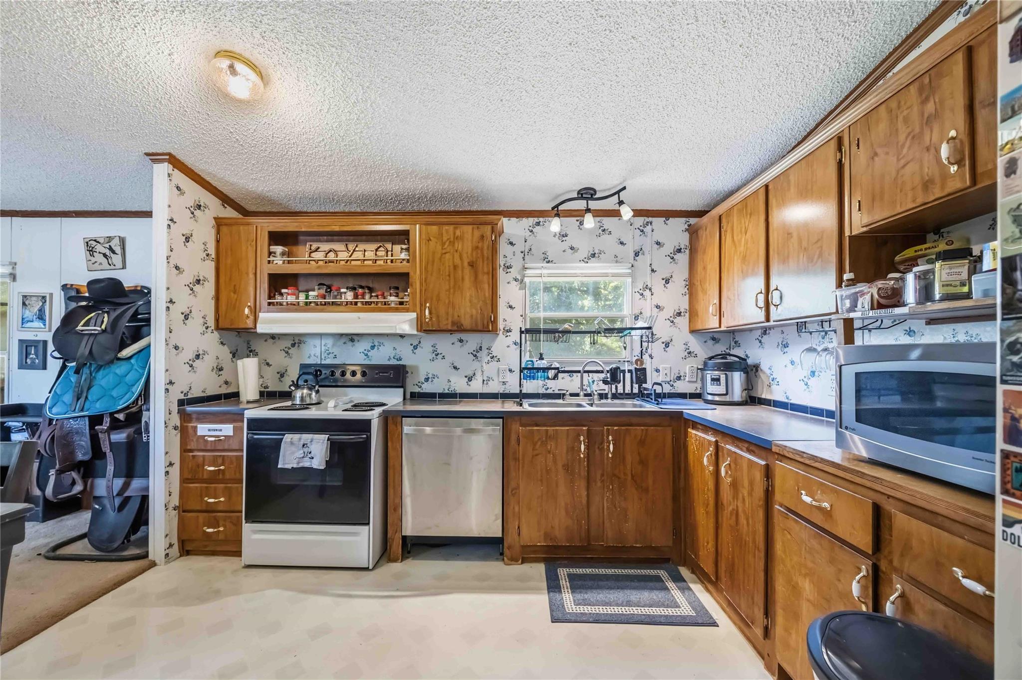 Kitchen with wood cabinets, floral wallpaper, and a saddle visible in the adjoining room.