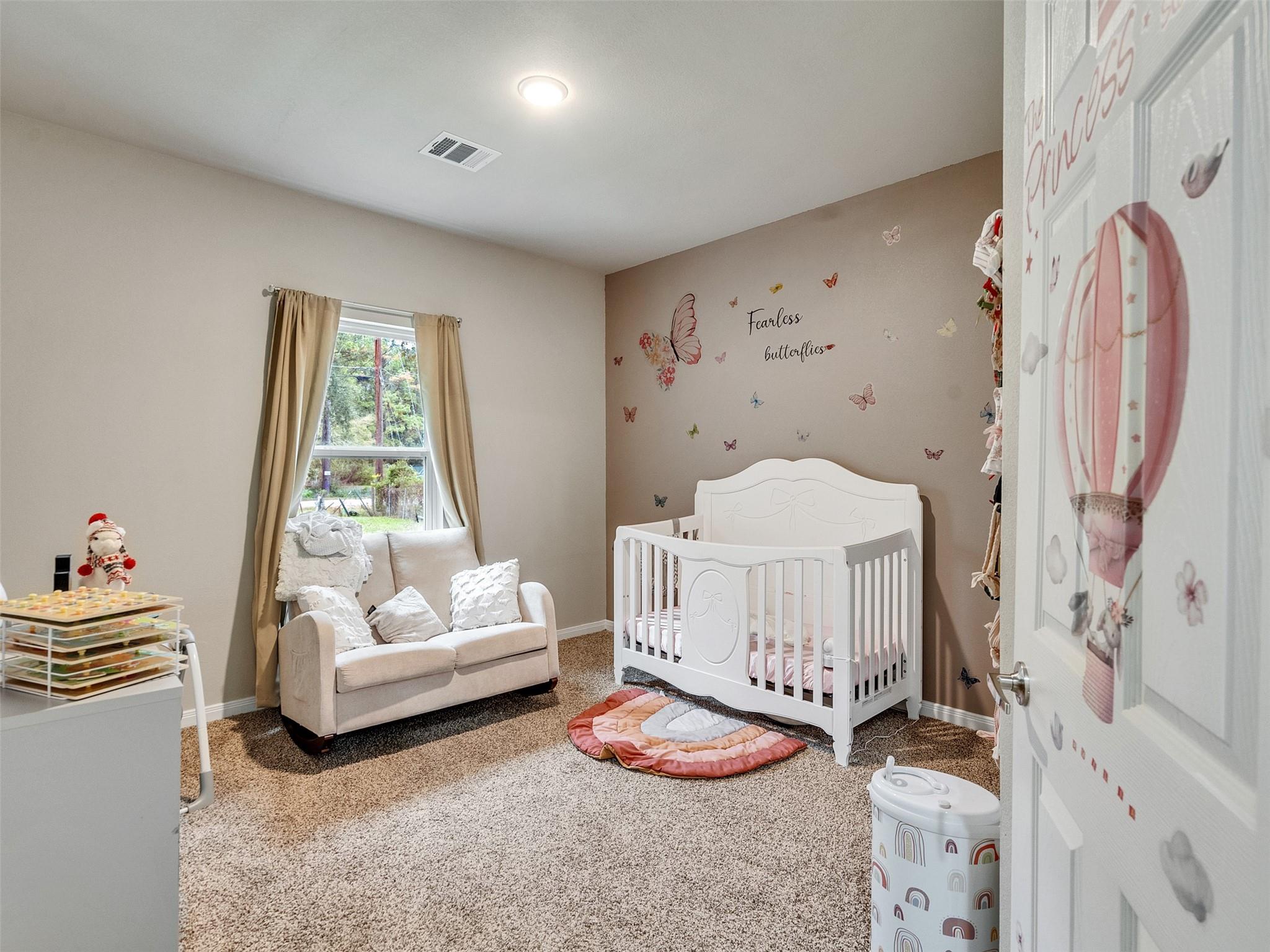 Nursery with a white crib, butterfly wall decals, and a loveseat beside the window.