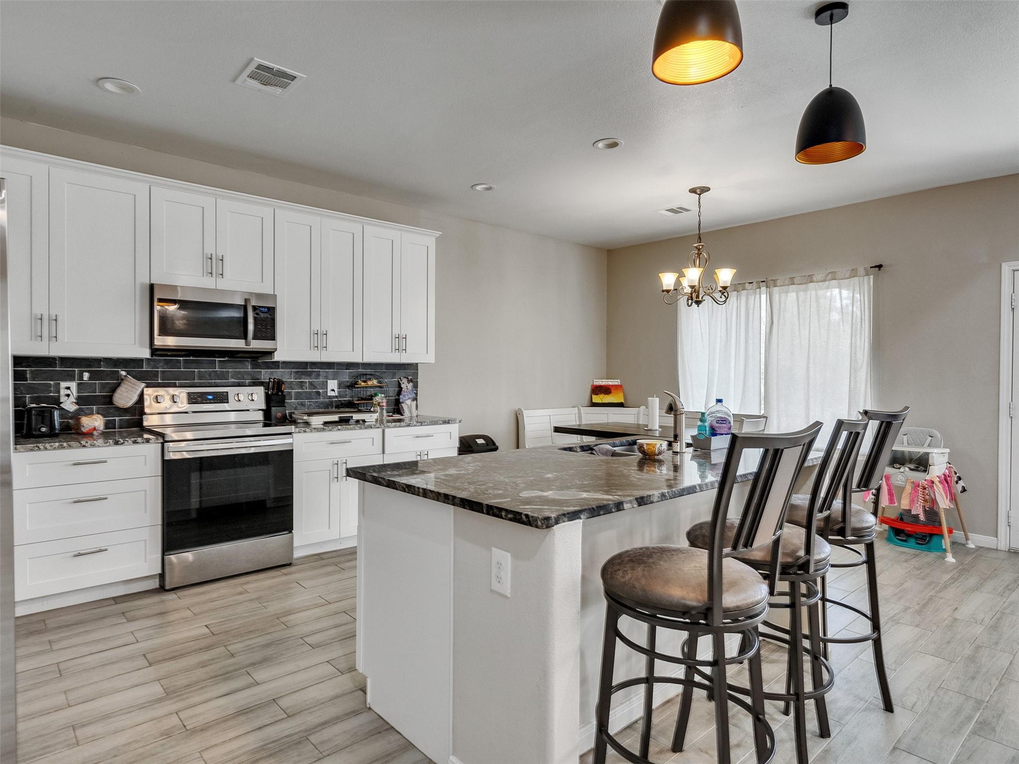 Kitchen with white cabinets, stainless appliances, and a large island with bar stools beside the dining area.