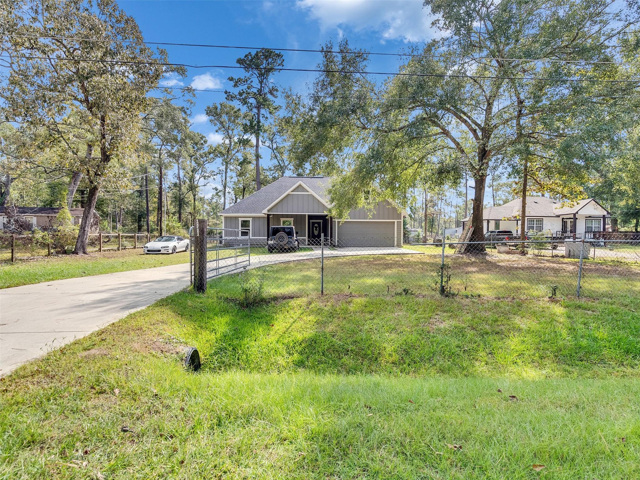 Gray single-story home with a two-car garage behind a chain-link fence and grassy yard.