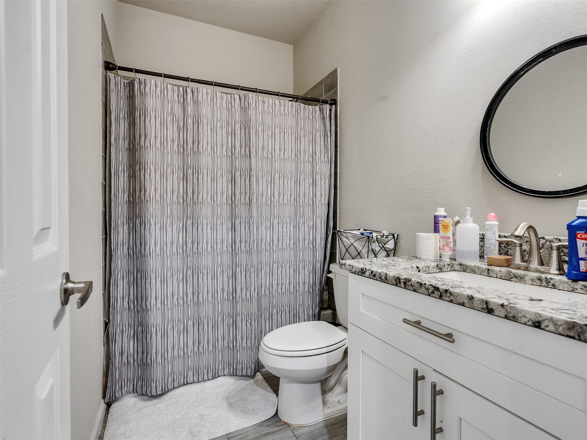 Bathroom with a gray patterned shower curtain, white vanity, and large round mirror.