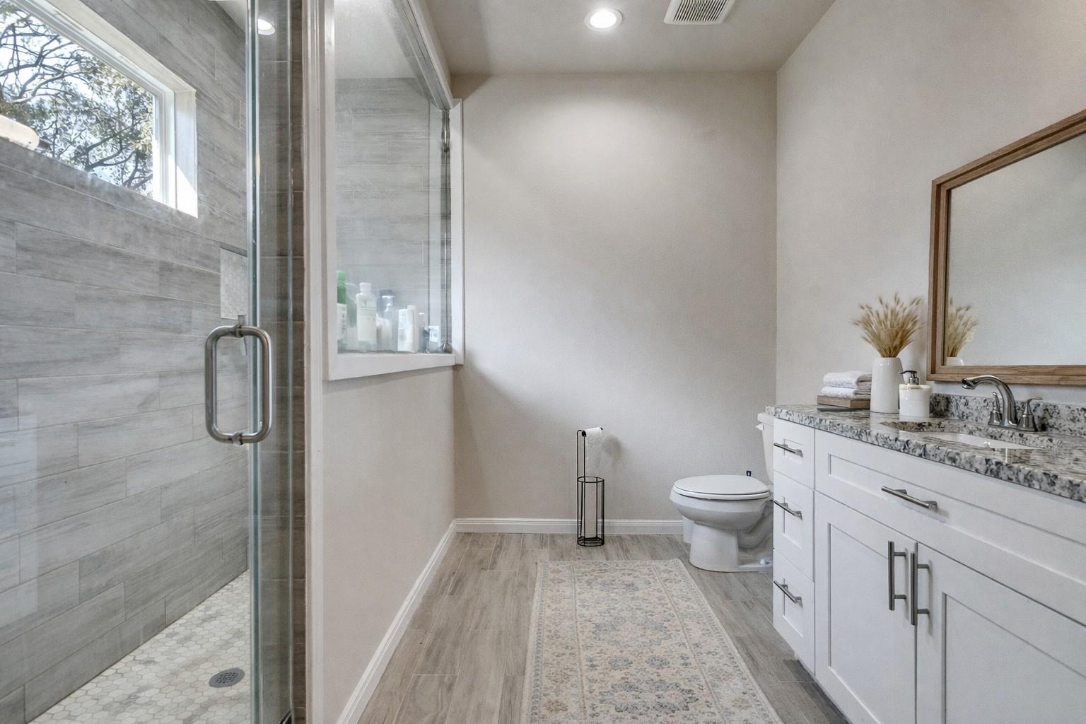 Bathroom with a tiled glass shower, white vanity, and window.