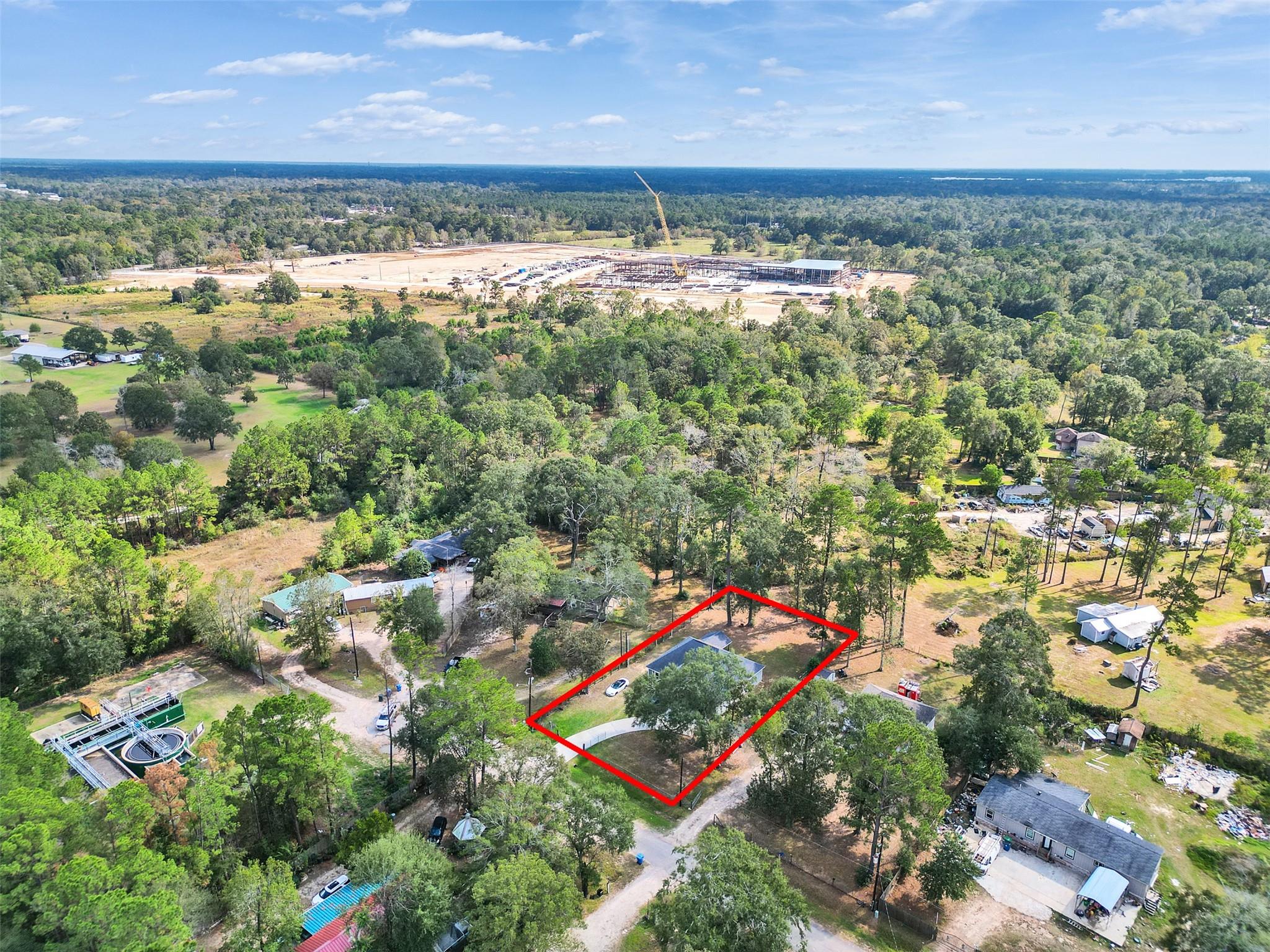 Aerial view of a tree-shaded home and its red-outlined lot, with a construction site in the distance.