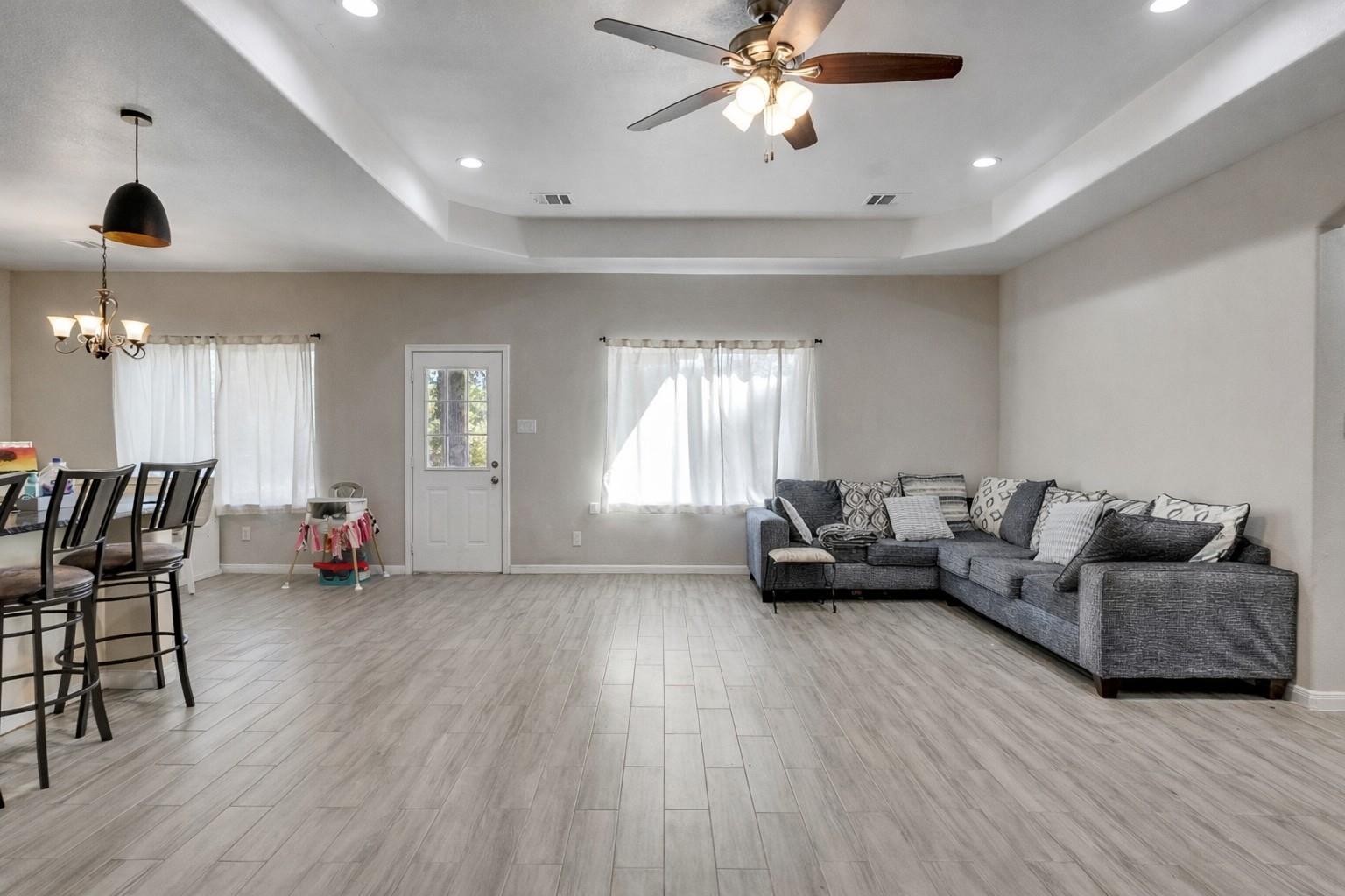 Living room with a gray sectional sofa, light tile floors, and an adjoining dining area.