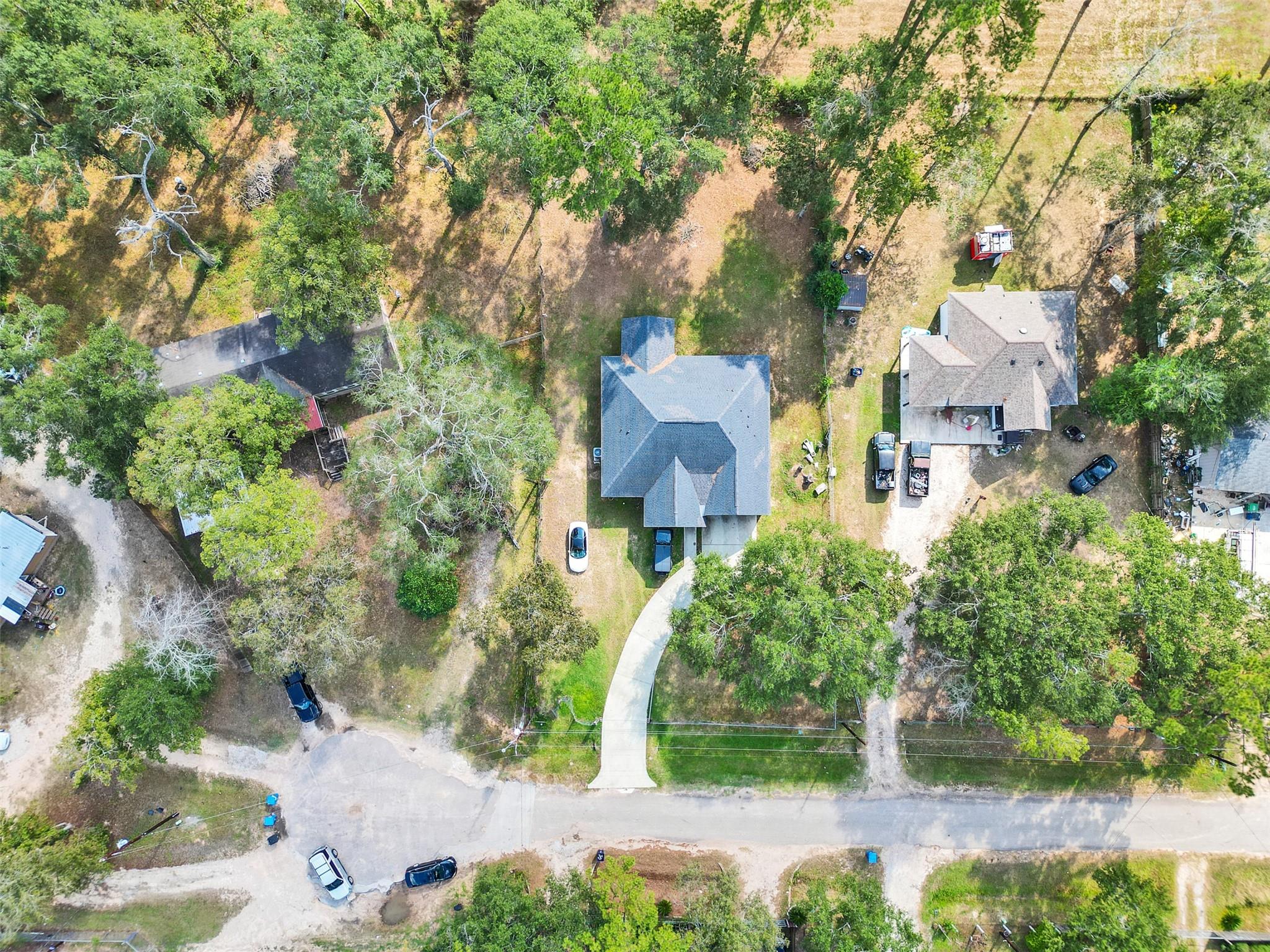 Aerial view of a gray-roofed home on a tree-covered lot with a curved driveway.