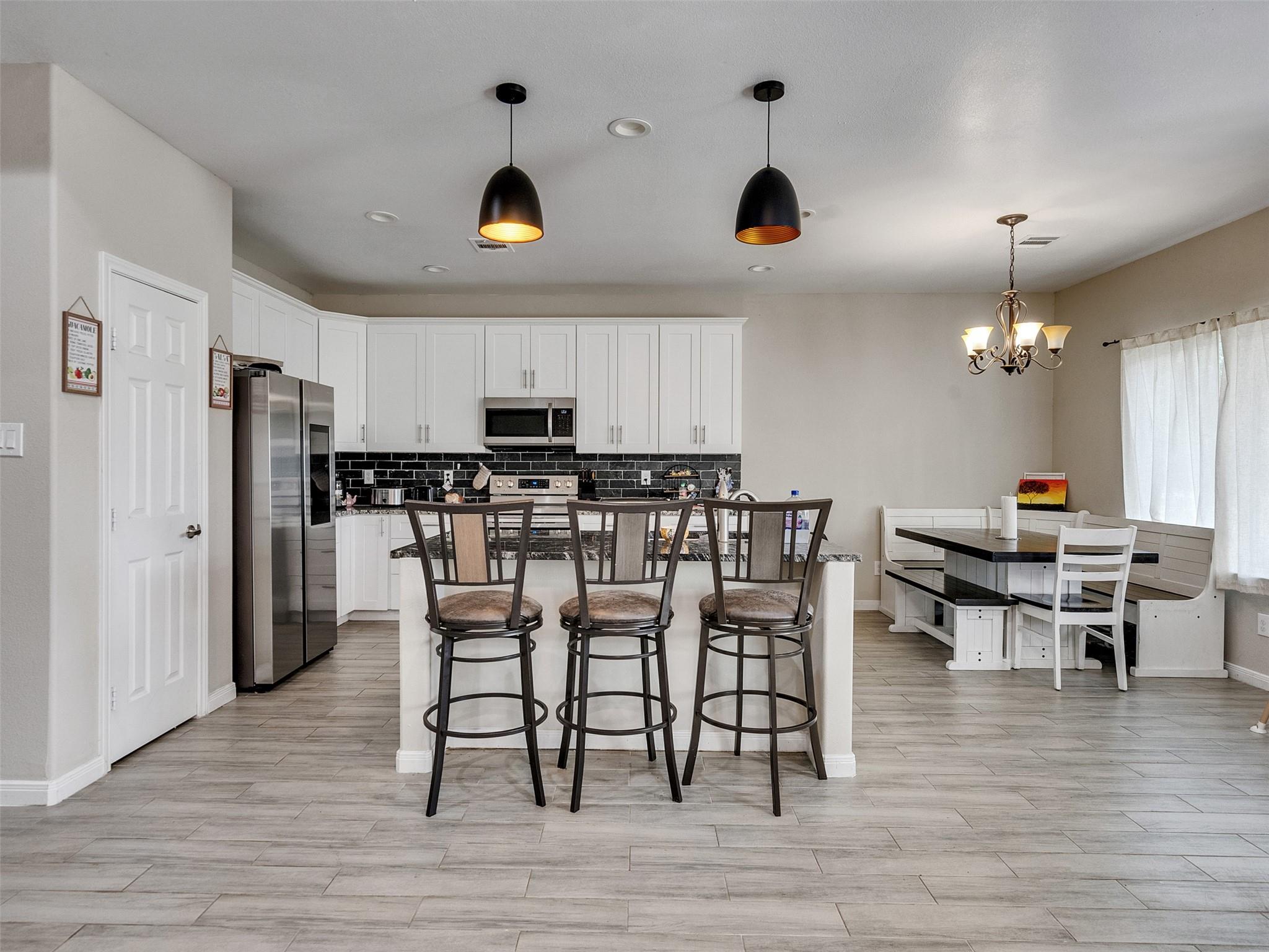 Open-plan kitchen with white cabinets and island, adjoining a dining nook with a window.
