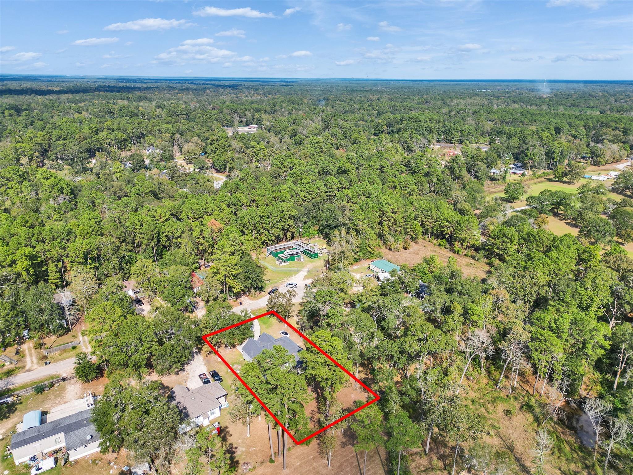 Aerial view of a wooded property outlined in red, with a house amid dense trees.