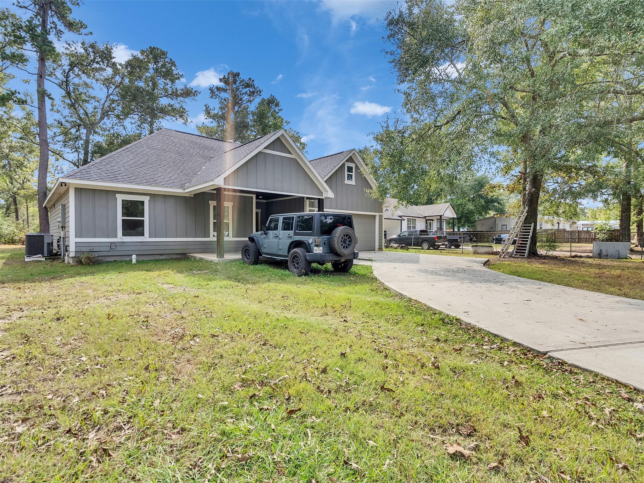 Gray single-story home with a covered entry and curved driveway, surrounded by mature trees.
