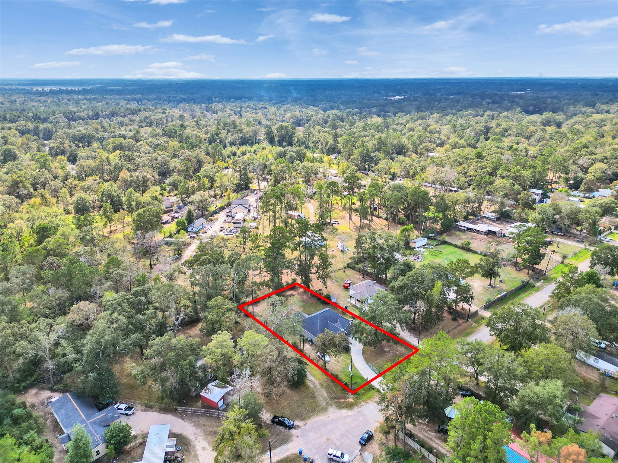Aerial view of a wooded residential lot outlined in red, with a house and curved driveway.