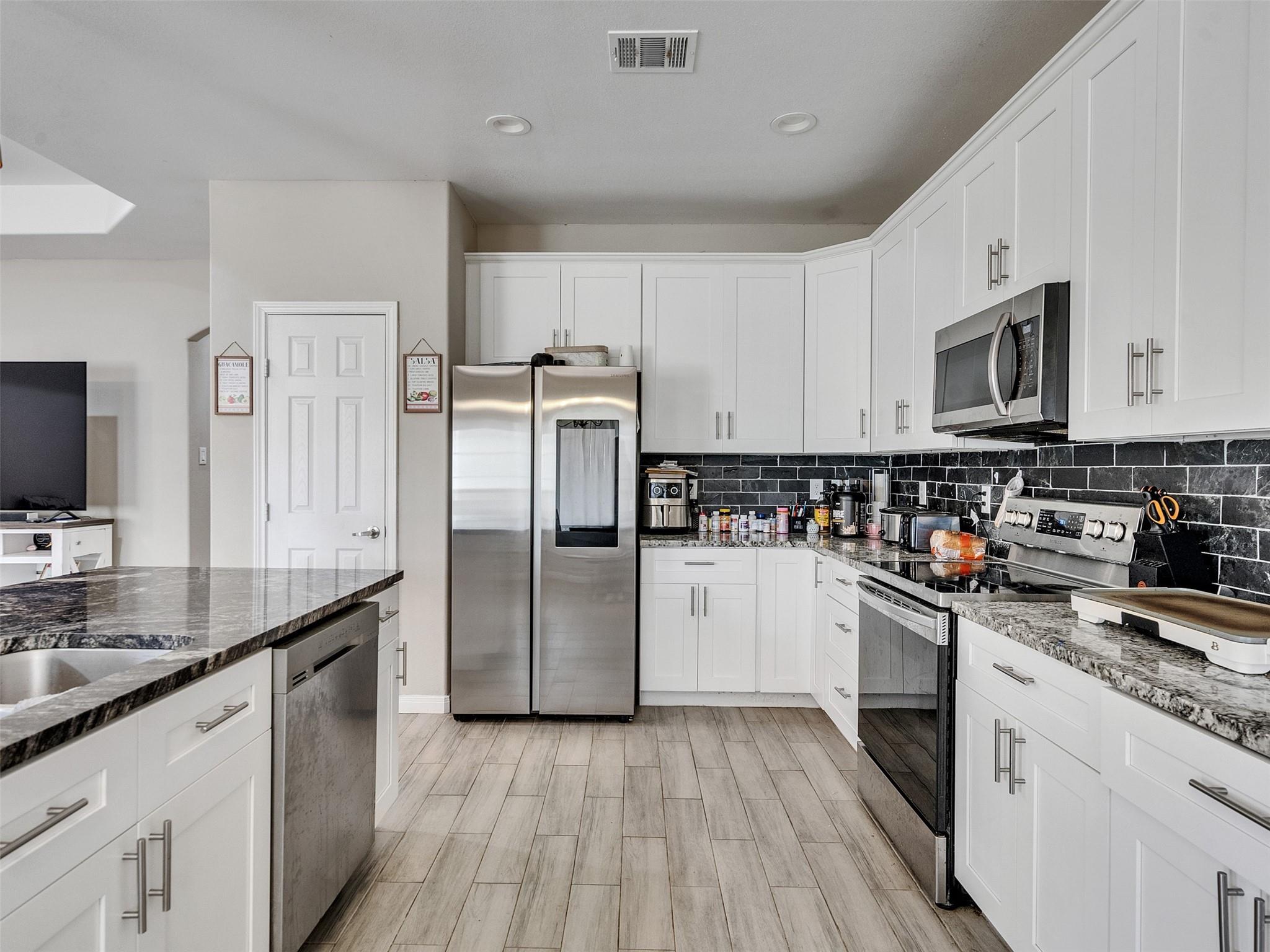 Kitchen with white cabinetry, dark stone counters and backsplash, and stainless steel appliances.